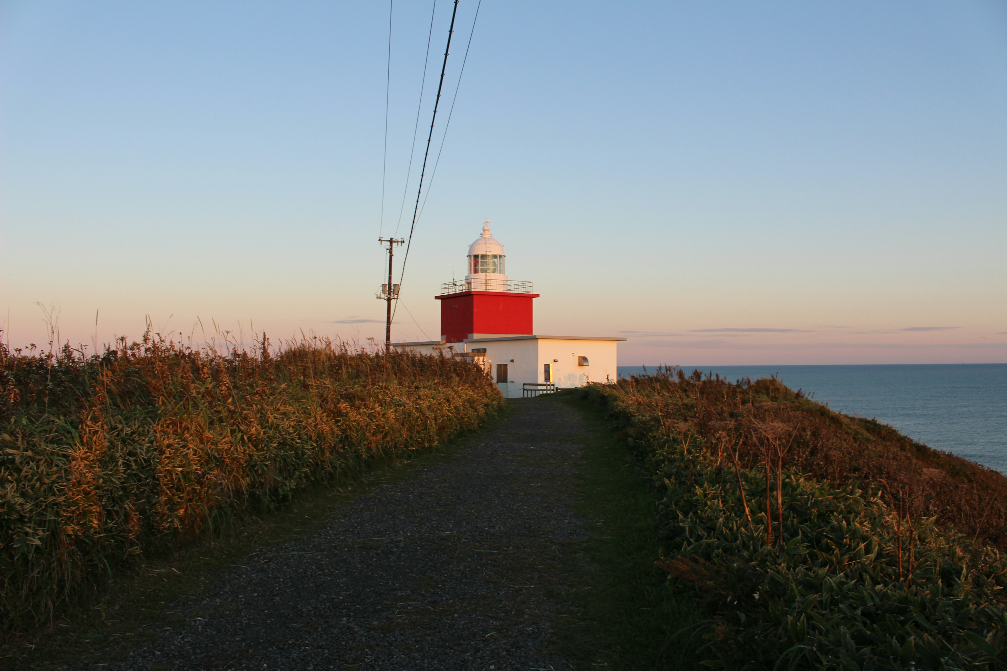 Red and white lighthouse by the sea with a grassy path