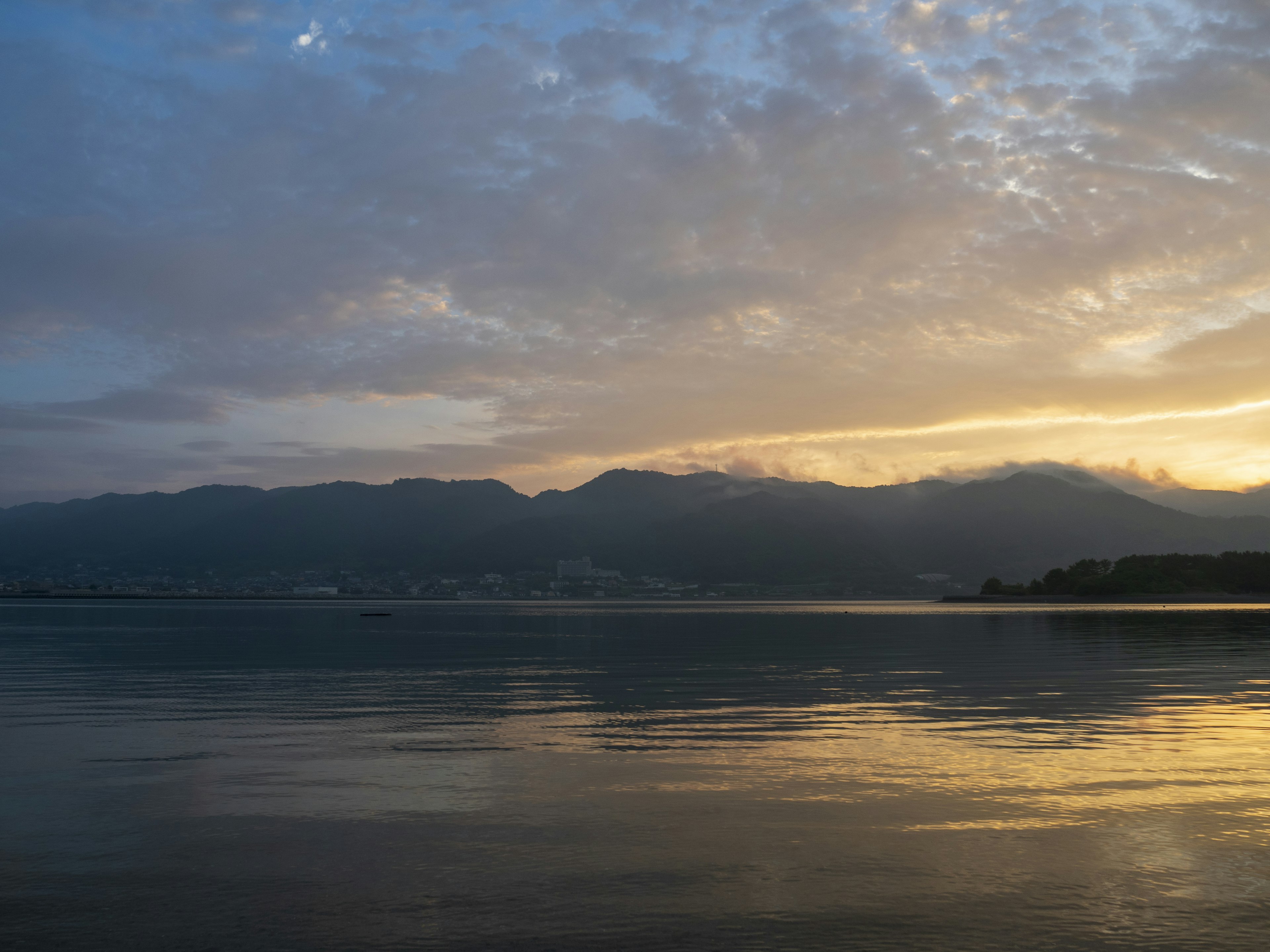 Danau tenang yang memantulkan matahari terbenam dan awan yang indah