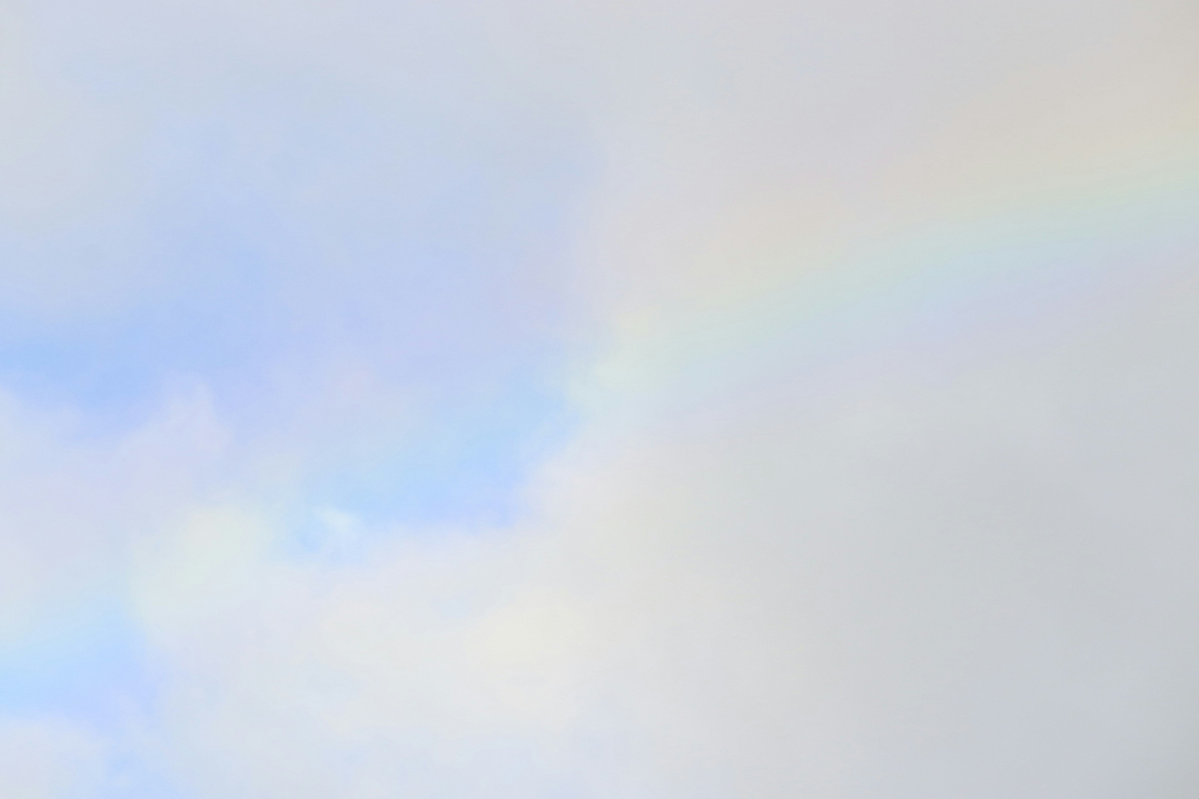 A faint rainbow appearing among light clouds and a blue sky