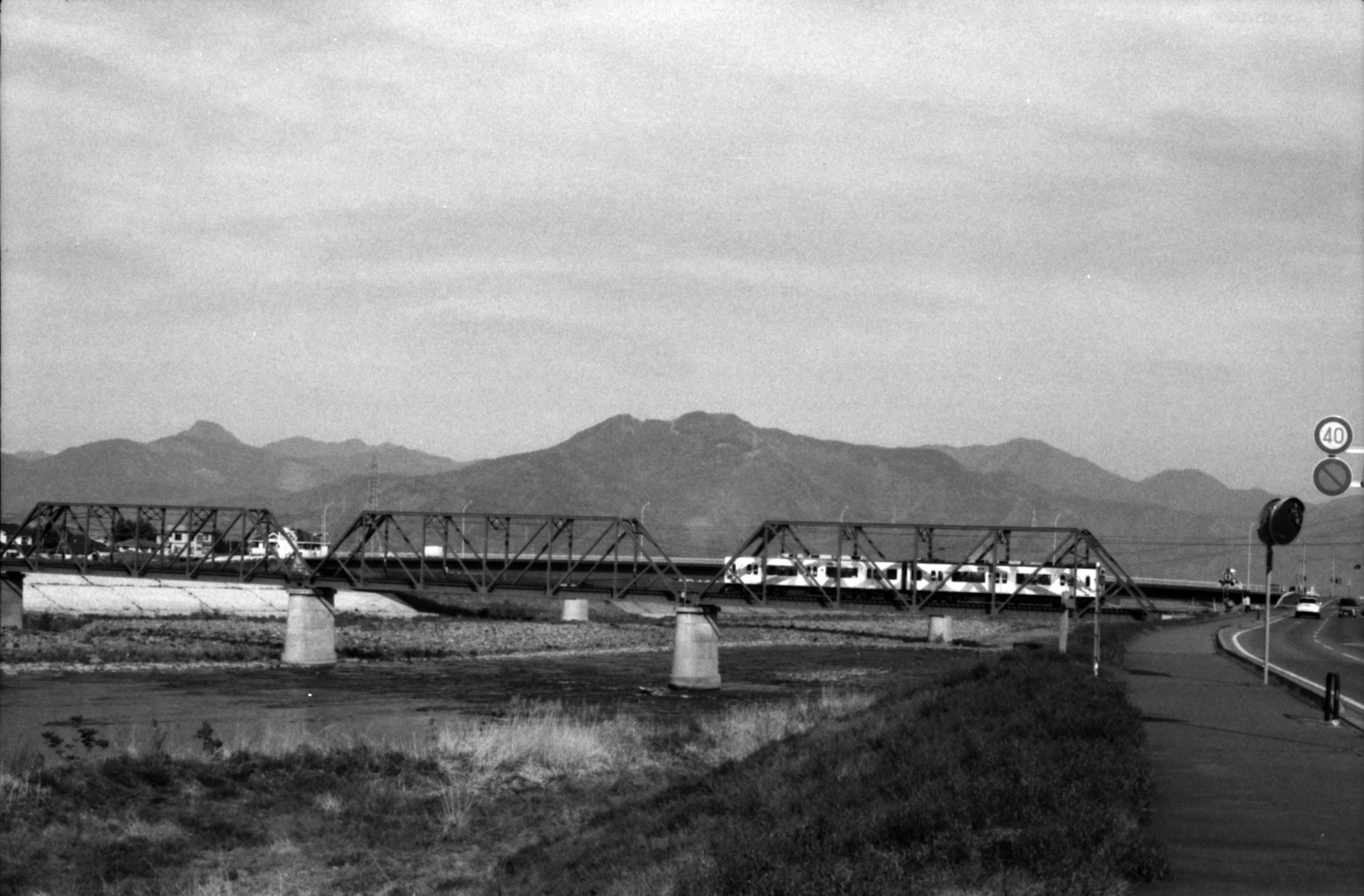 Treno in bianco e nero che attraversa un ponte ferroviario con montagne sullo sfondo