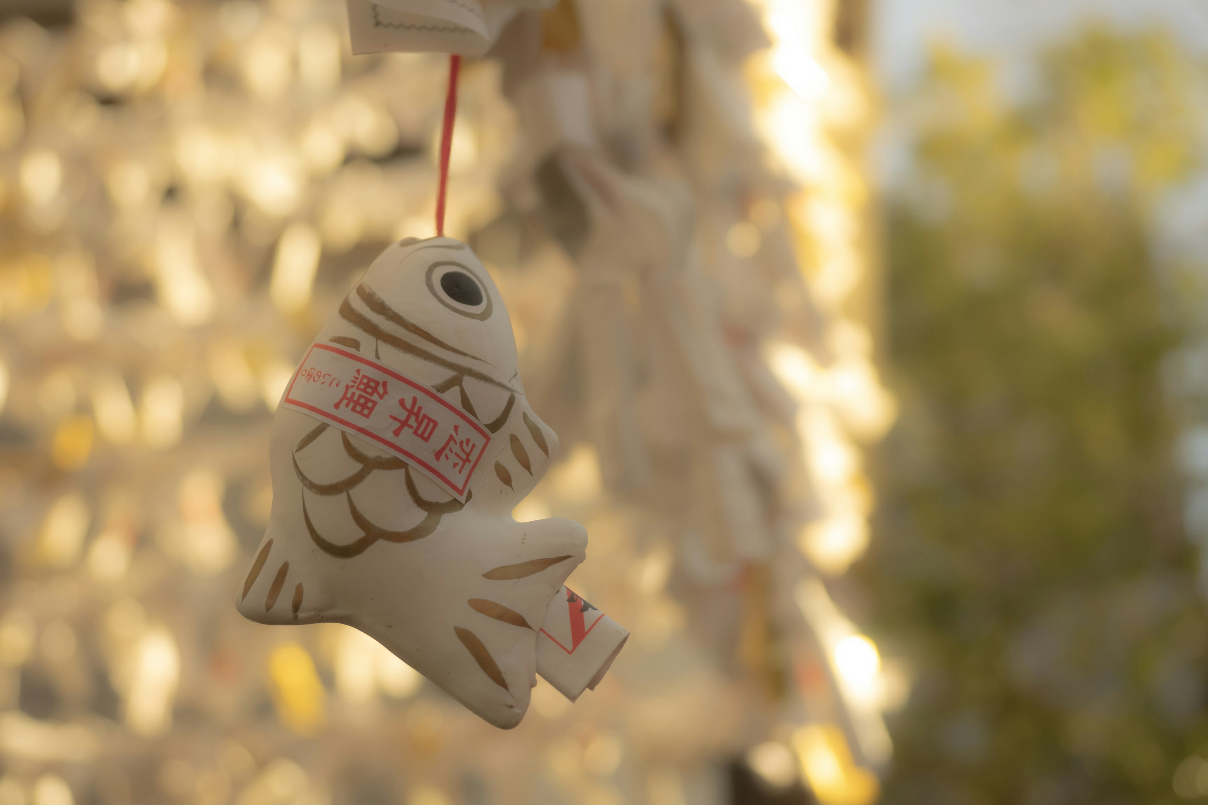 A white fish-shaped ornament hanging with blurred decorations in the background