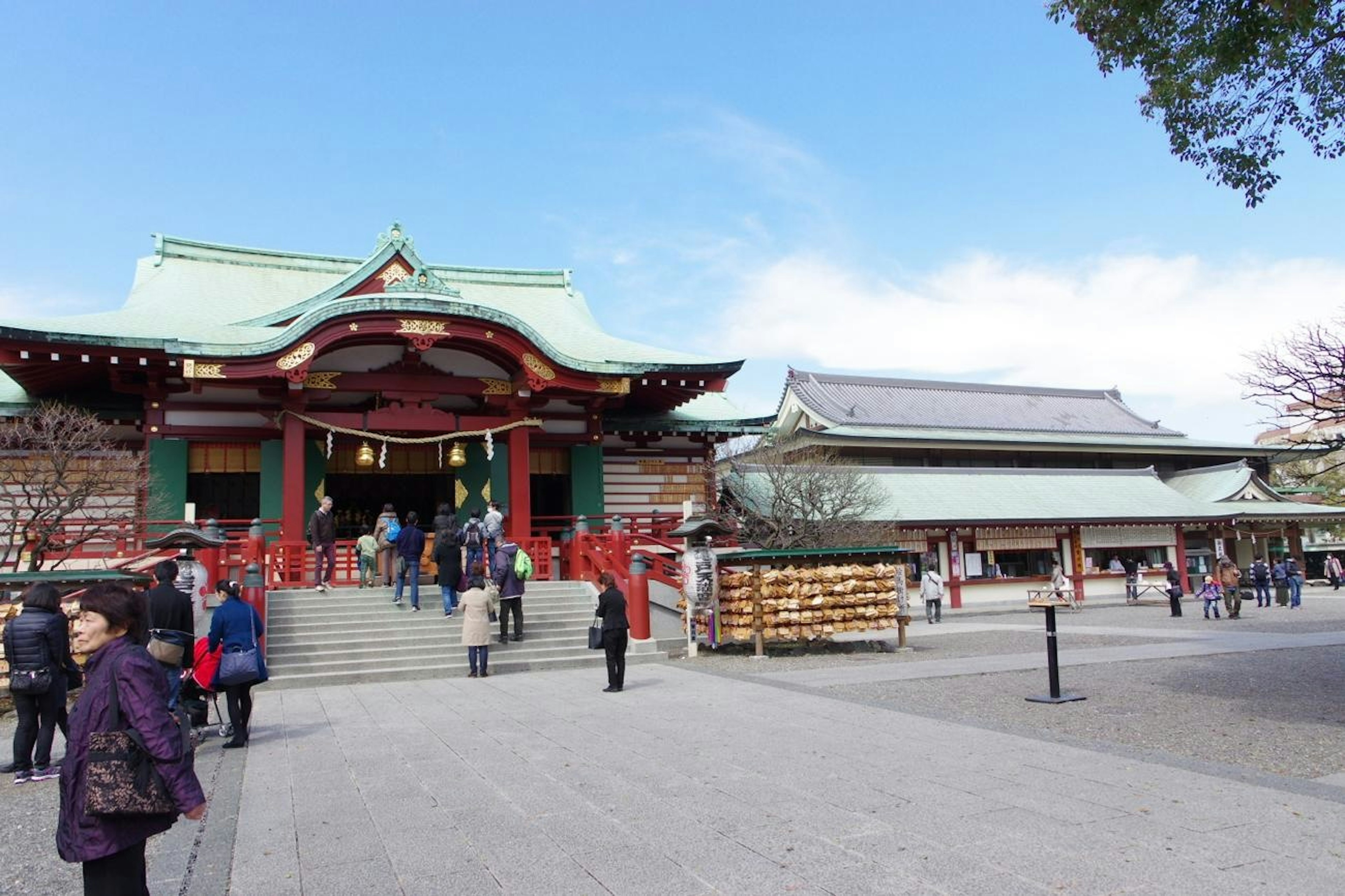 Shrine with red pillars and green roof surrounded by visitors