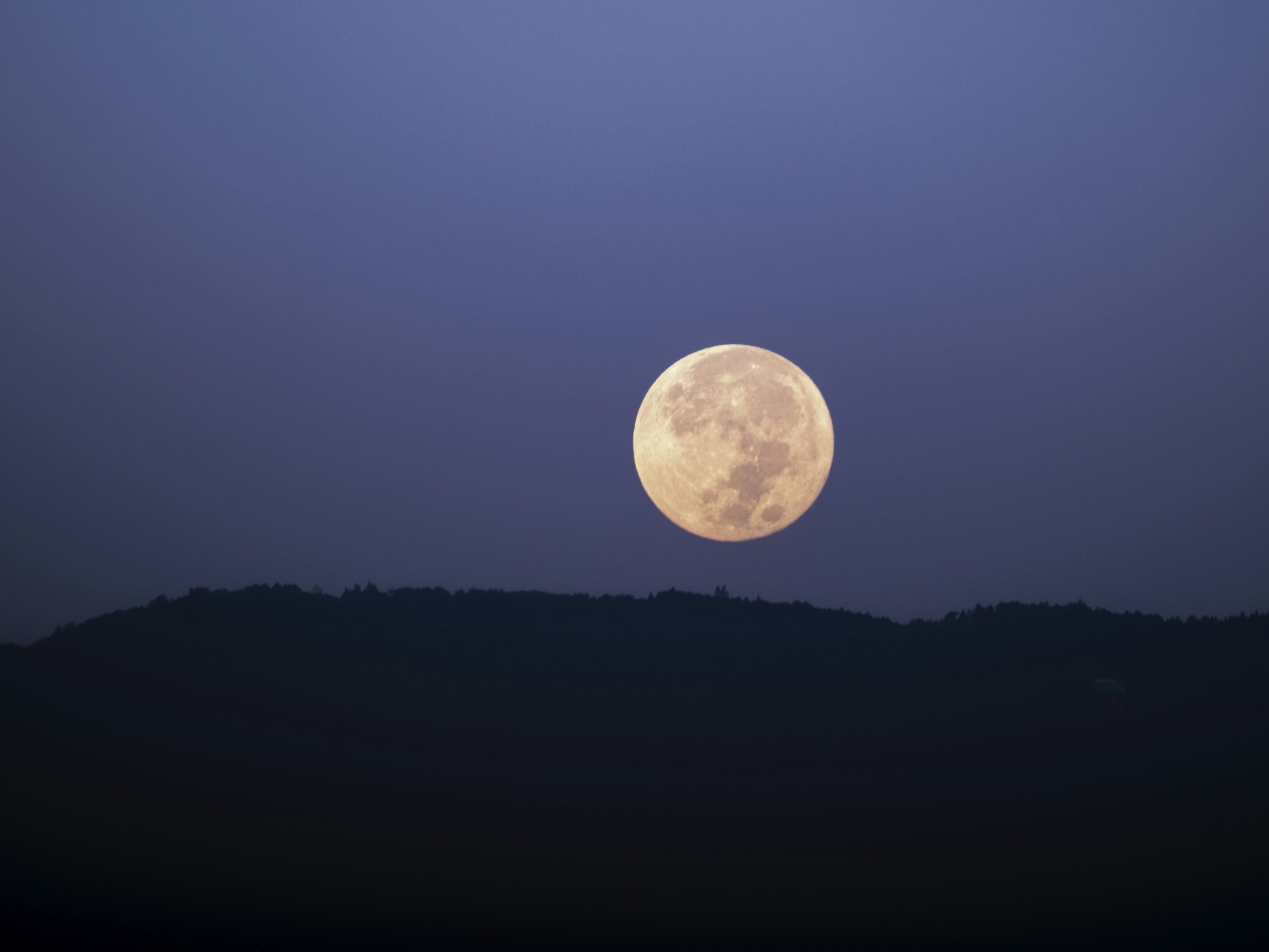 Full moon against a blue sky with mountain silhouette