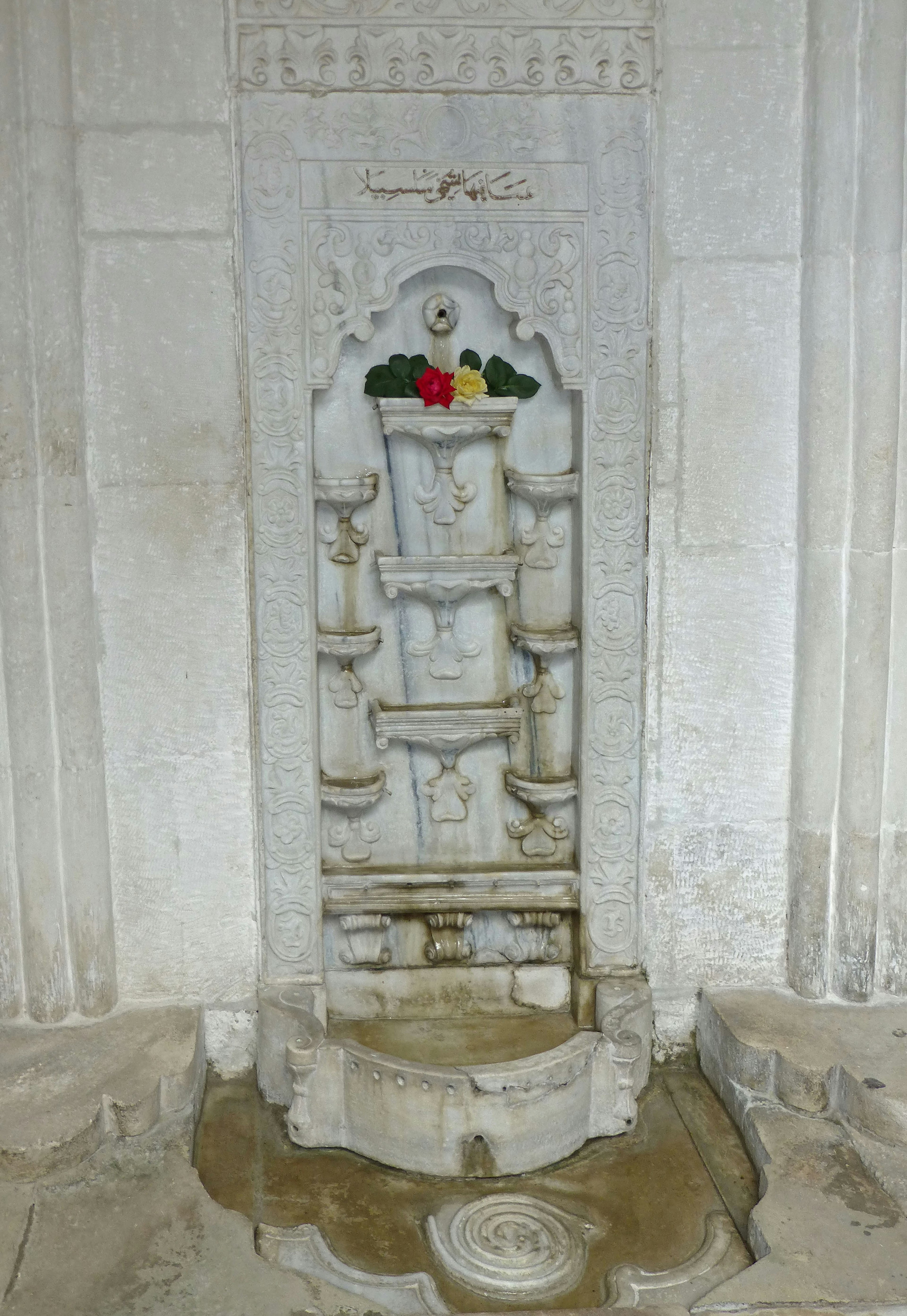 Weißer Steinbrunnen mit kunstvollen Wanddekorationen in rot und grün