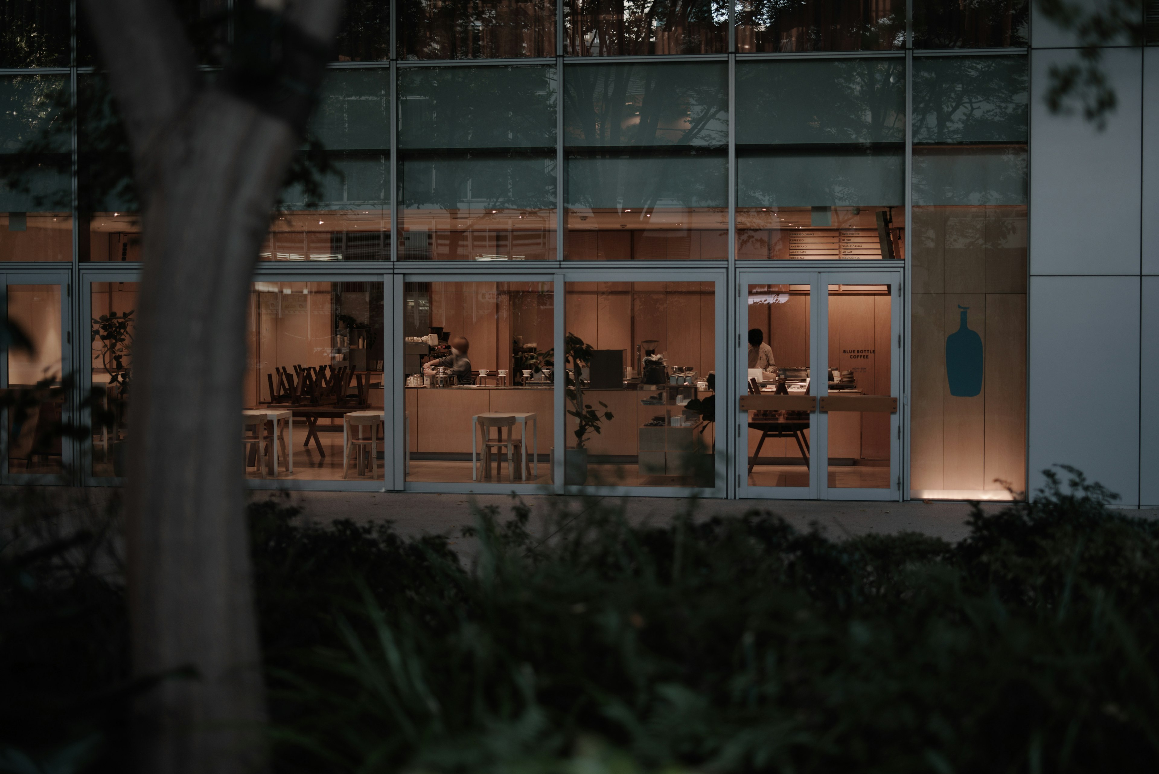 Interior view of a cafe at night visible through the windows featuring chairs and tables in a cozy atmosphere