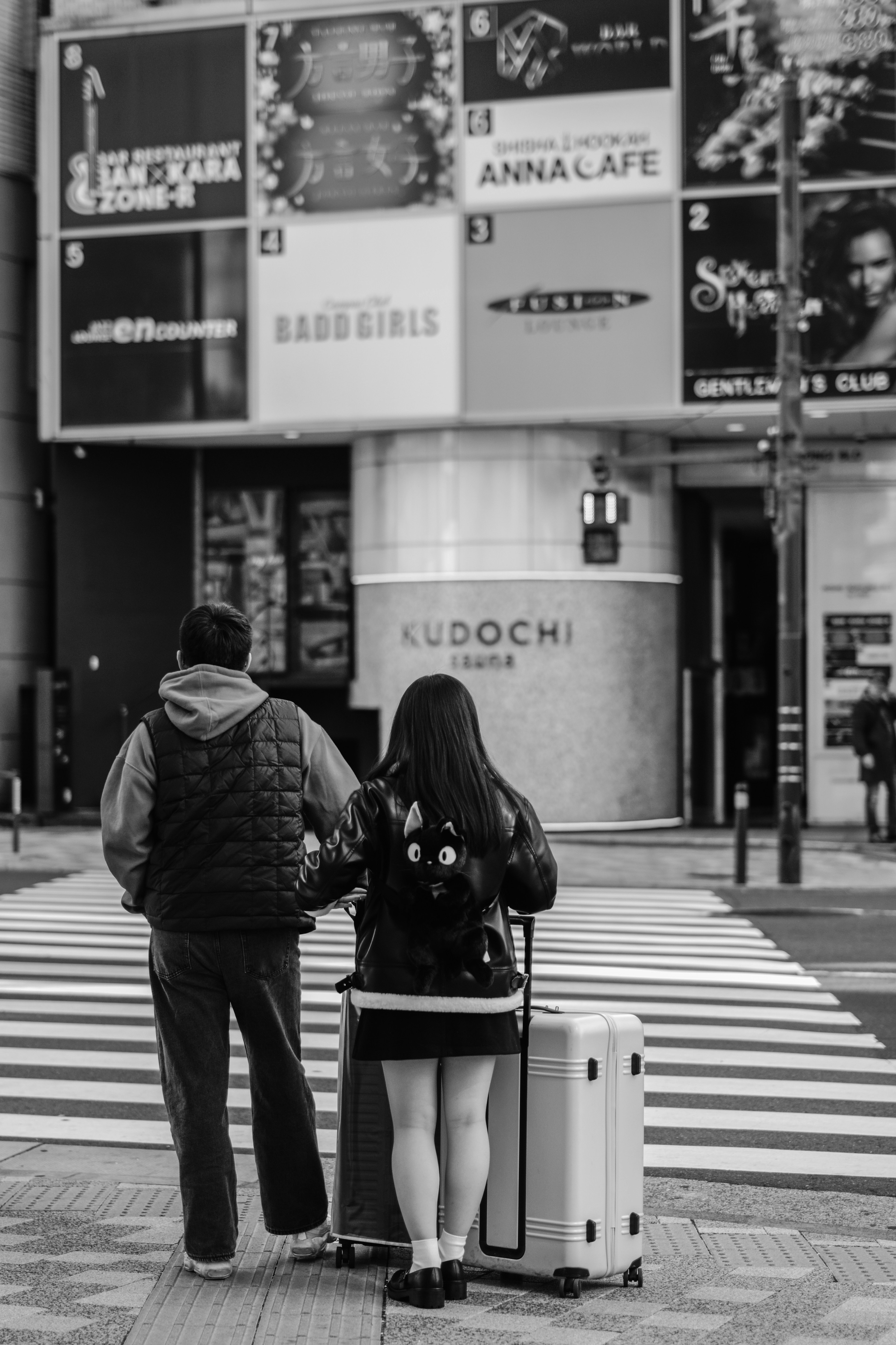 Two people standing at a crosswalk with a suitcase in a city