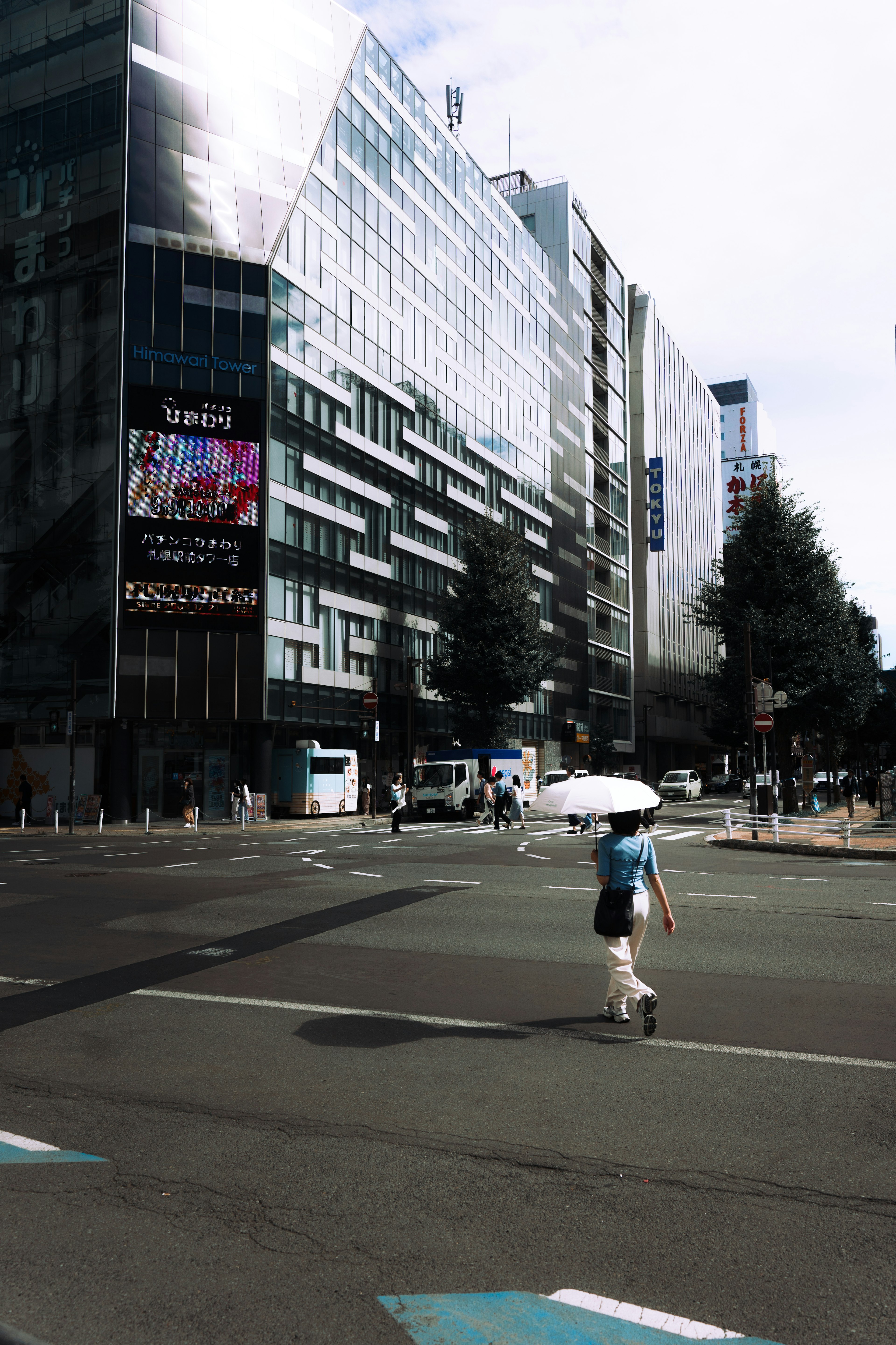 A person walking with an umbrella on a sunny street corner near modern buildings