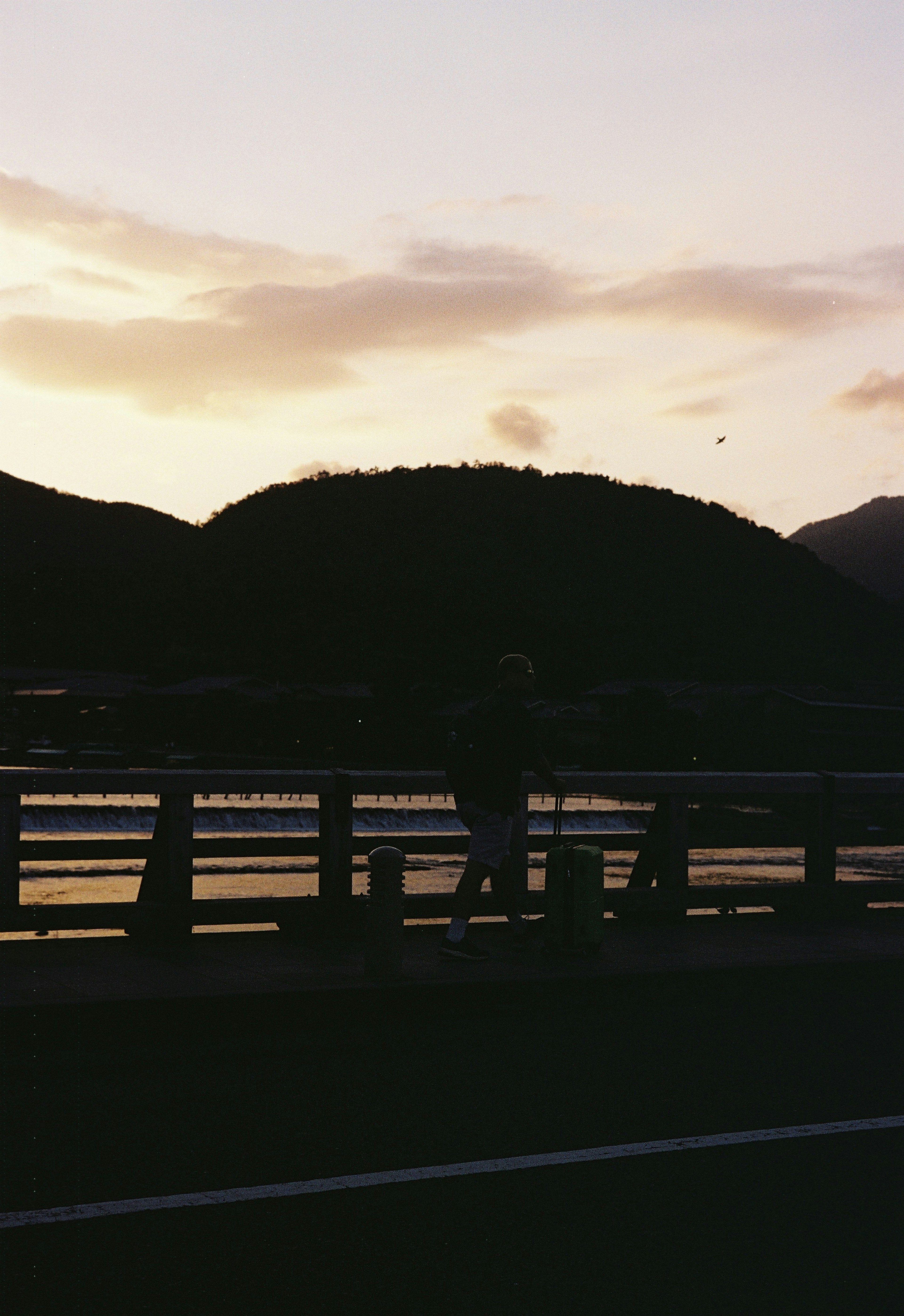 夕焼けの中で橋を歩く人のシルエットと山の風景