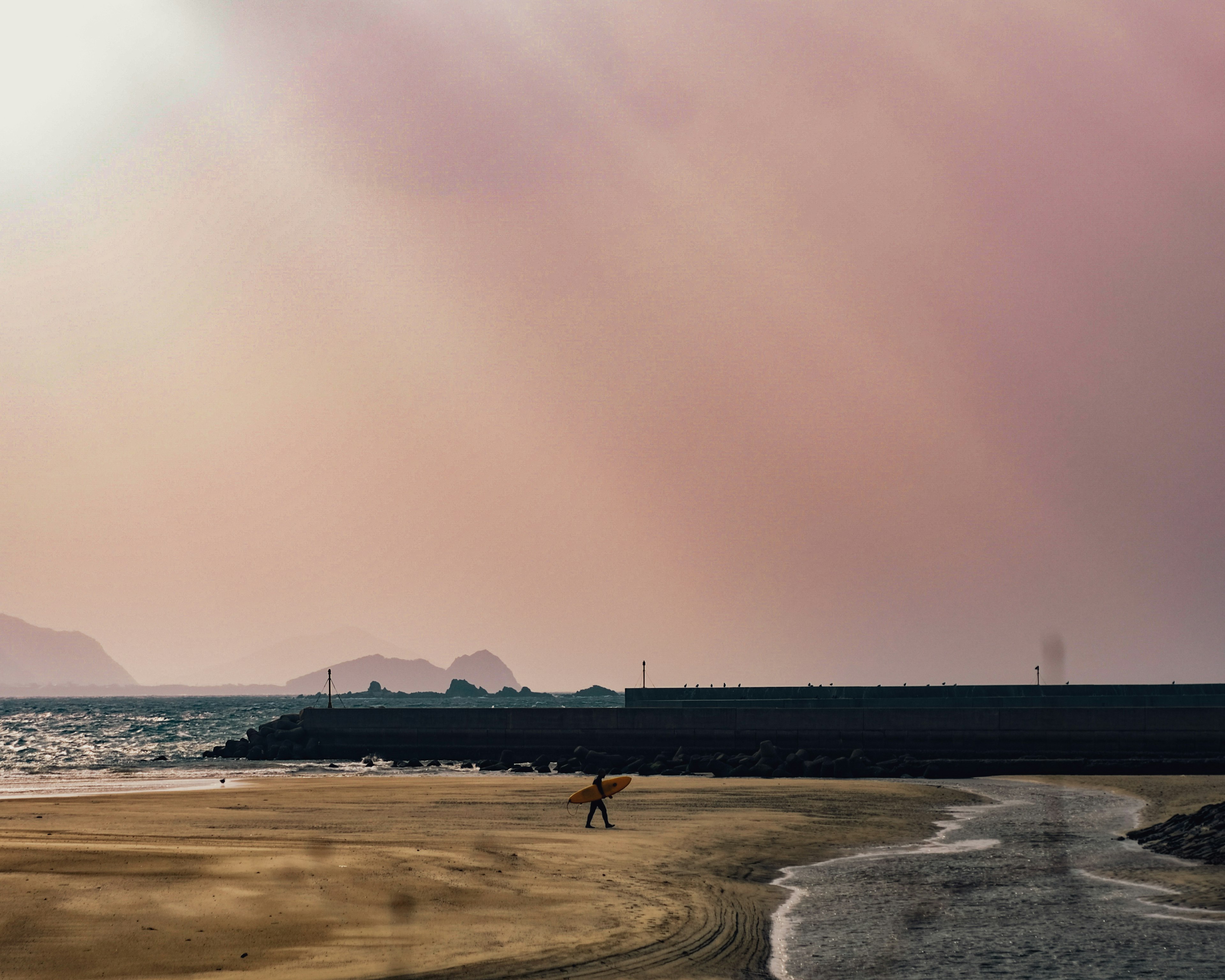 A person standing on a sandy beach with a tranquil sea backdrop during sunset