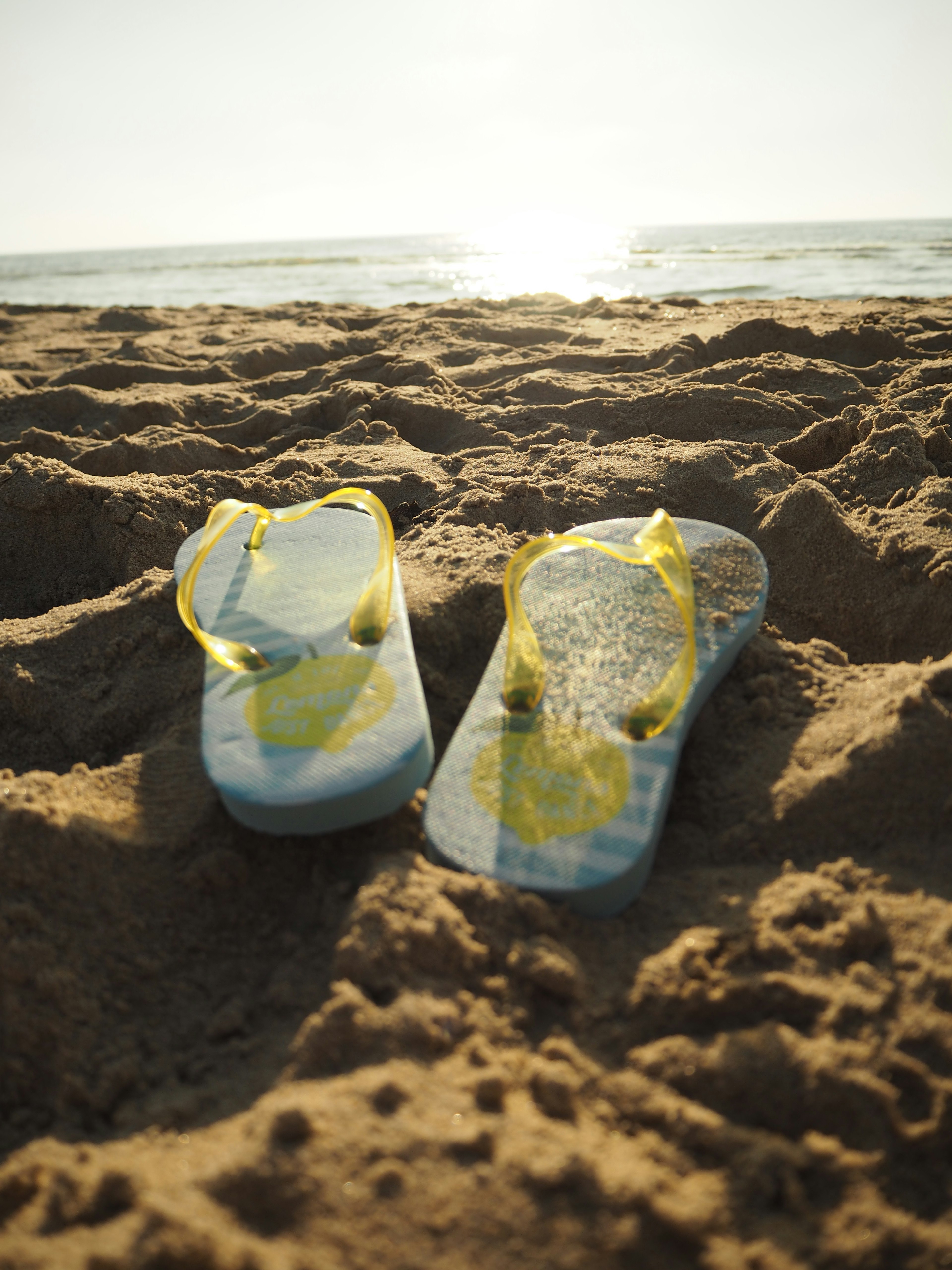 Flip-flop kuning di pantai berpasir dengan pemandangan laut