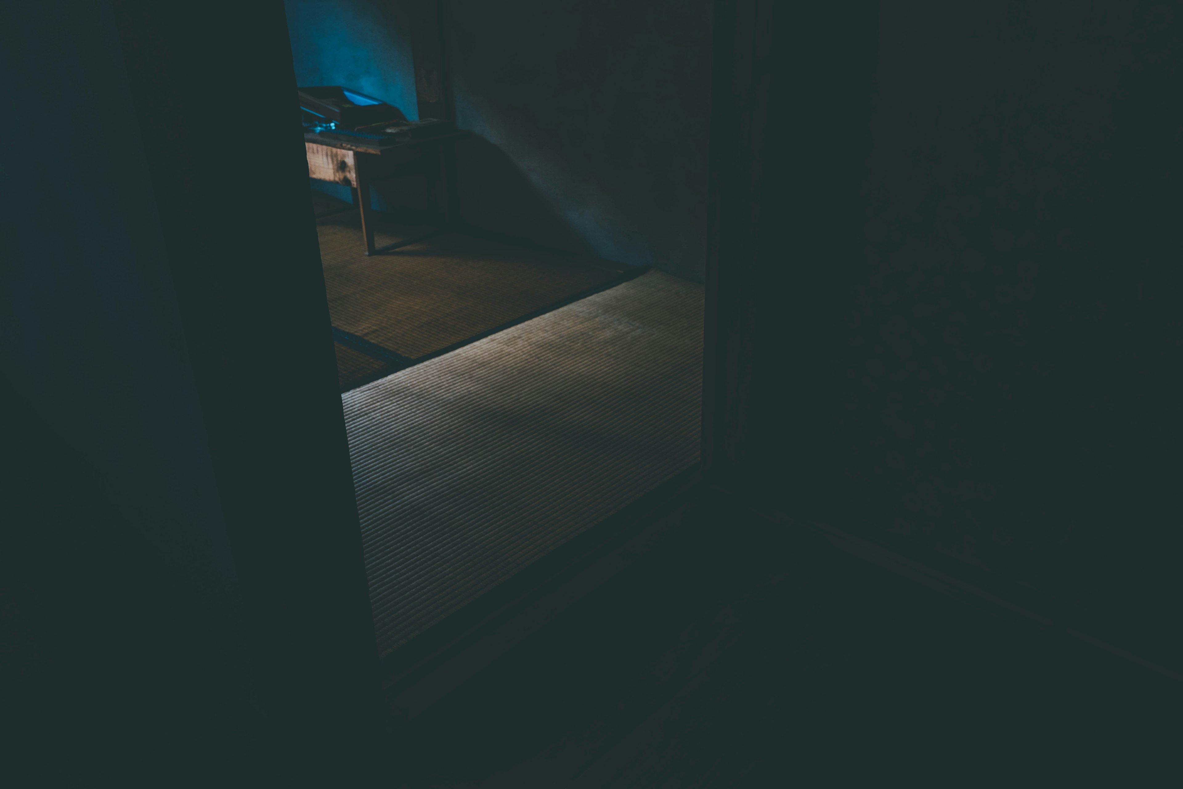 A glimpse of blue light from a dark room through a partially open door and illuminated floor