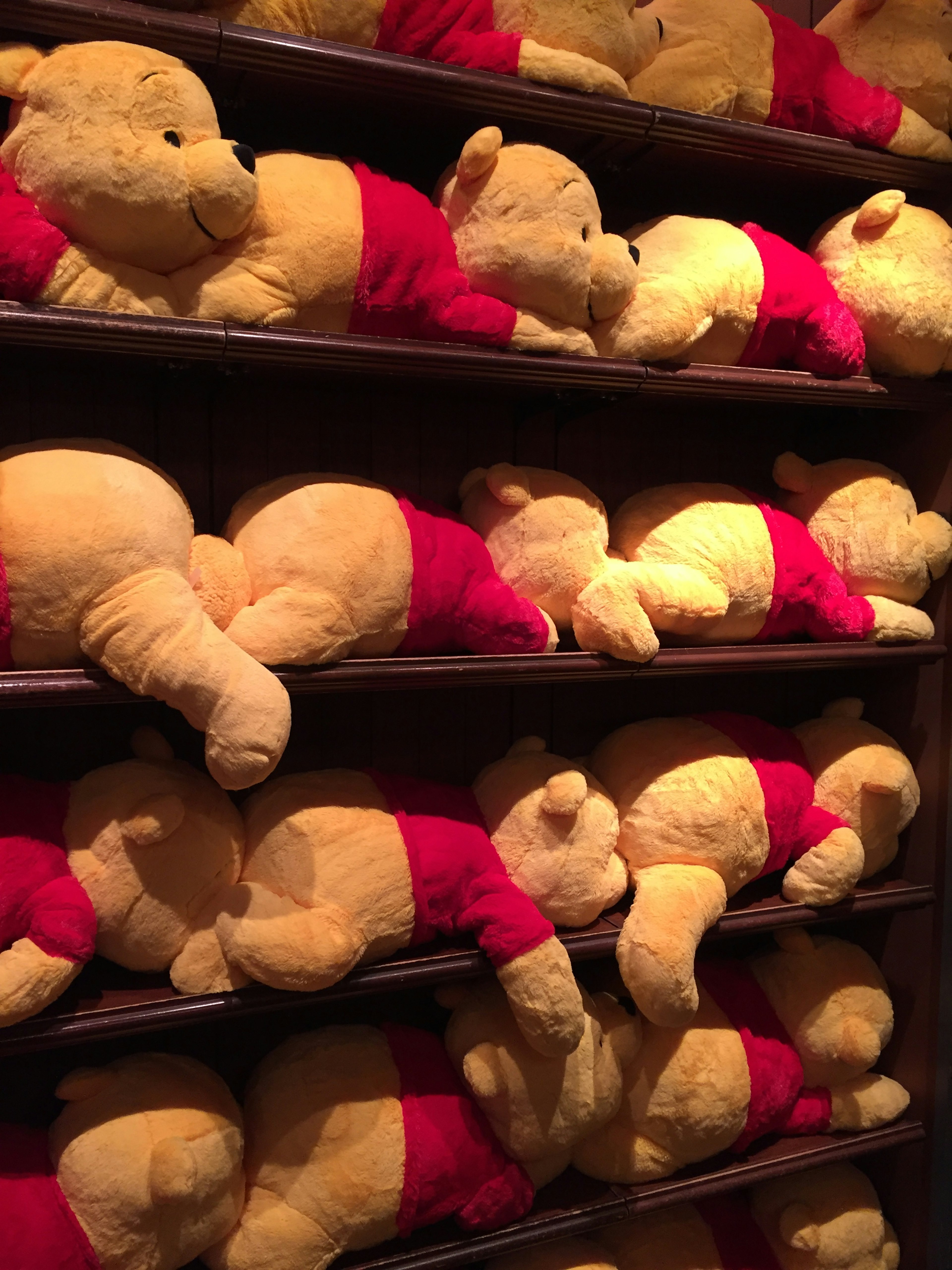 A row of plush Winnie the Pooh toys lying on shelves