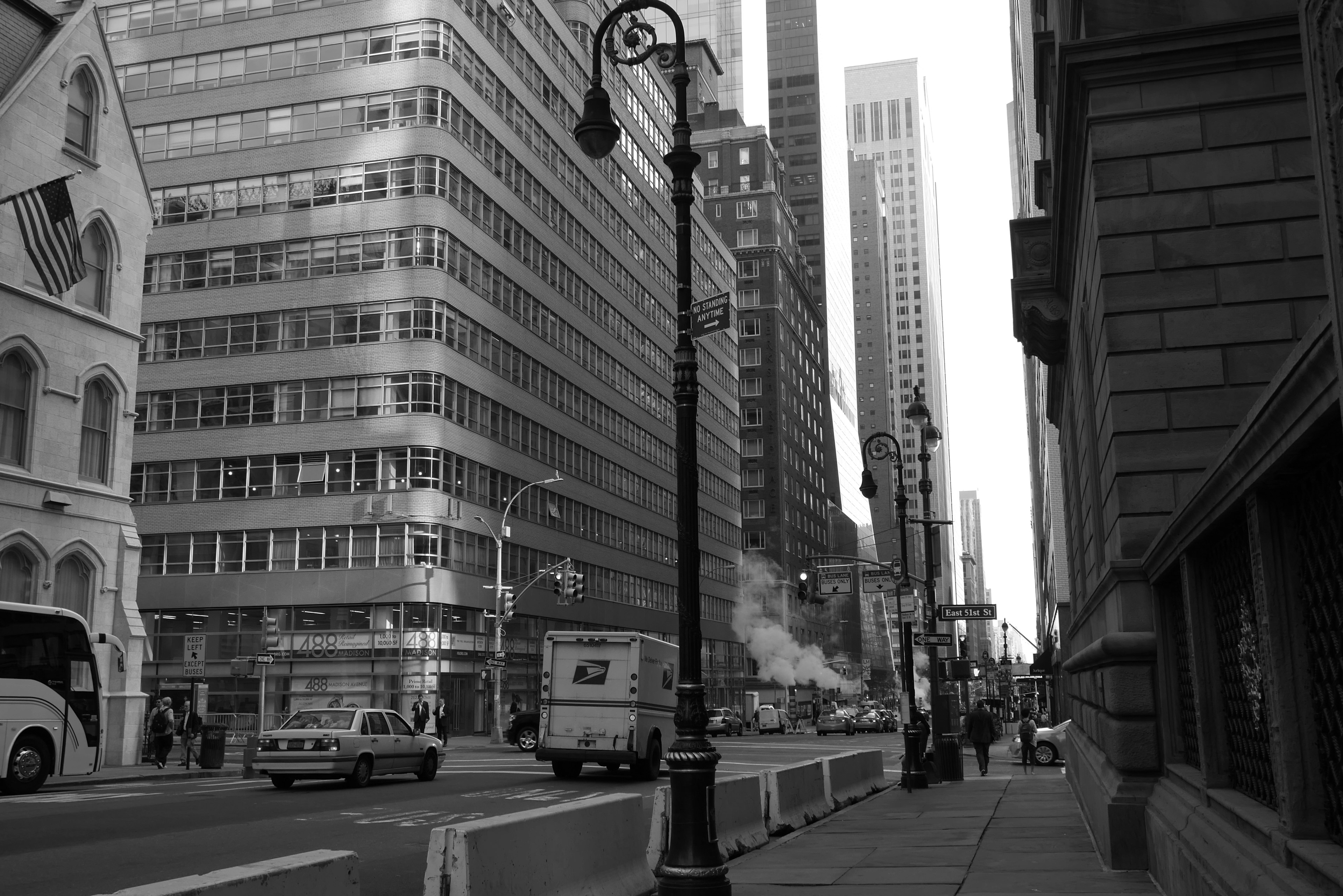 Black and white cityscape featuring tall buildings and street lamps with traffic