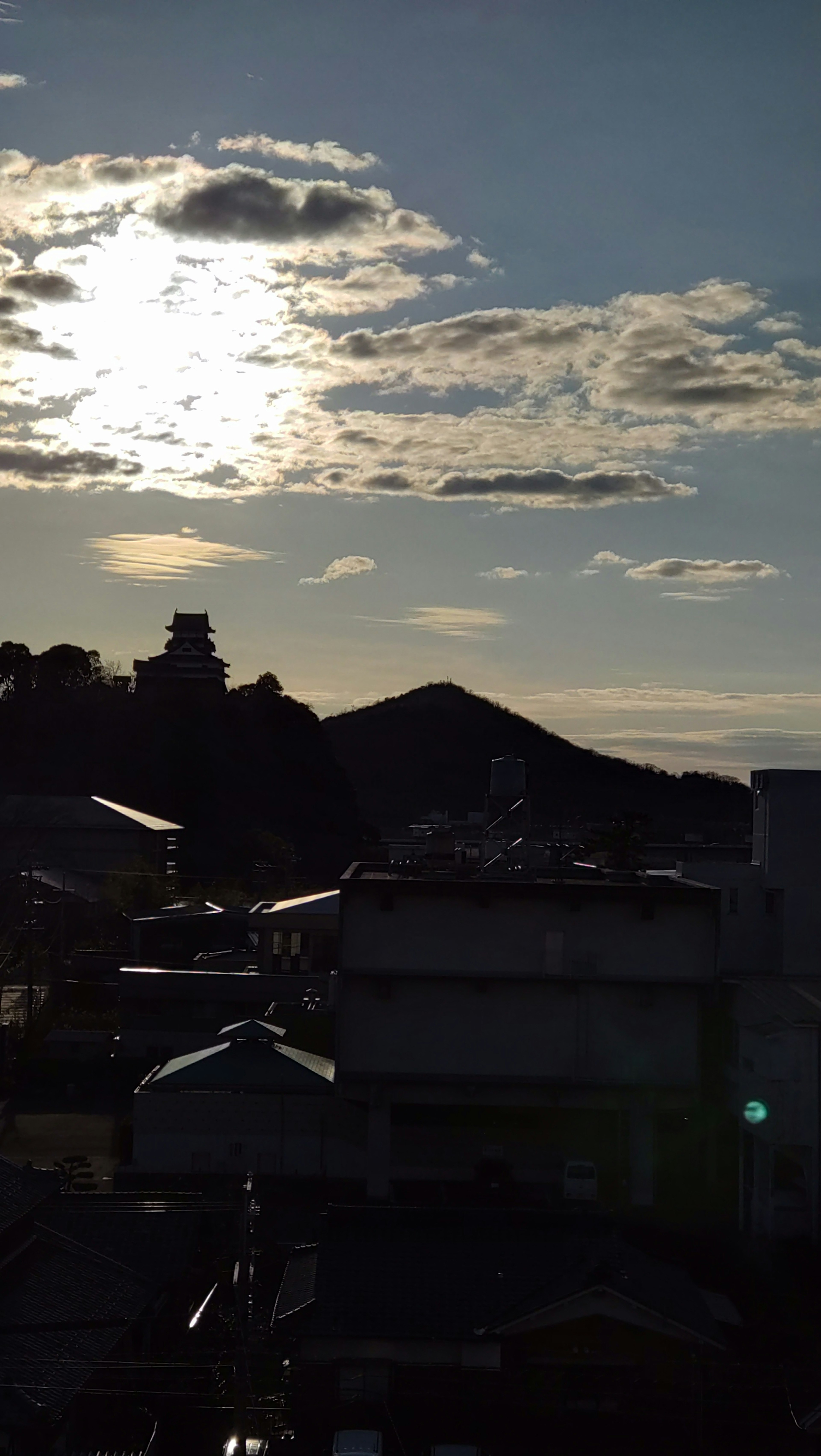 夕暮れの空に浮かぶ雲と太陽の光が反射するシルエットの山