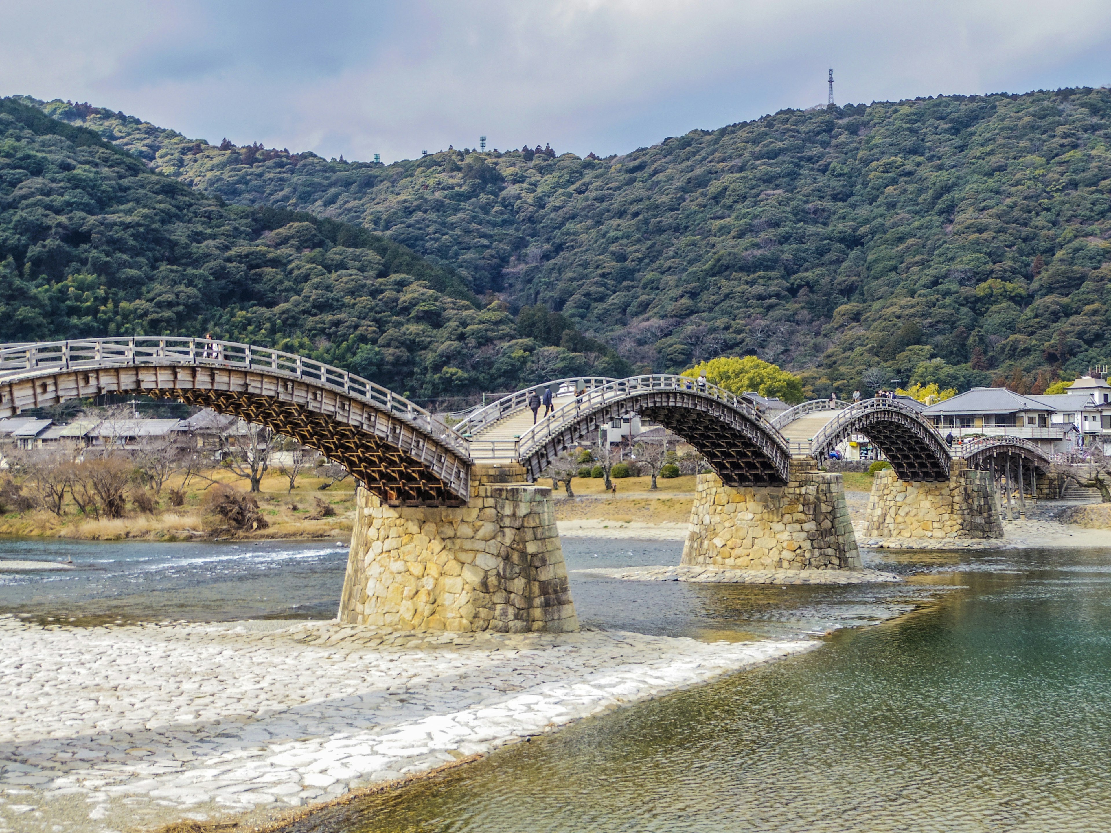 A beautiful wooden arch bridge spans a river surrounded by green mountains