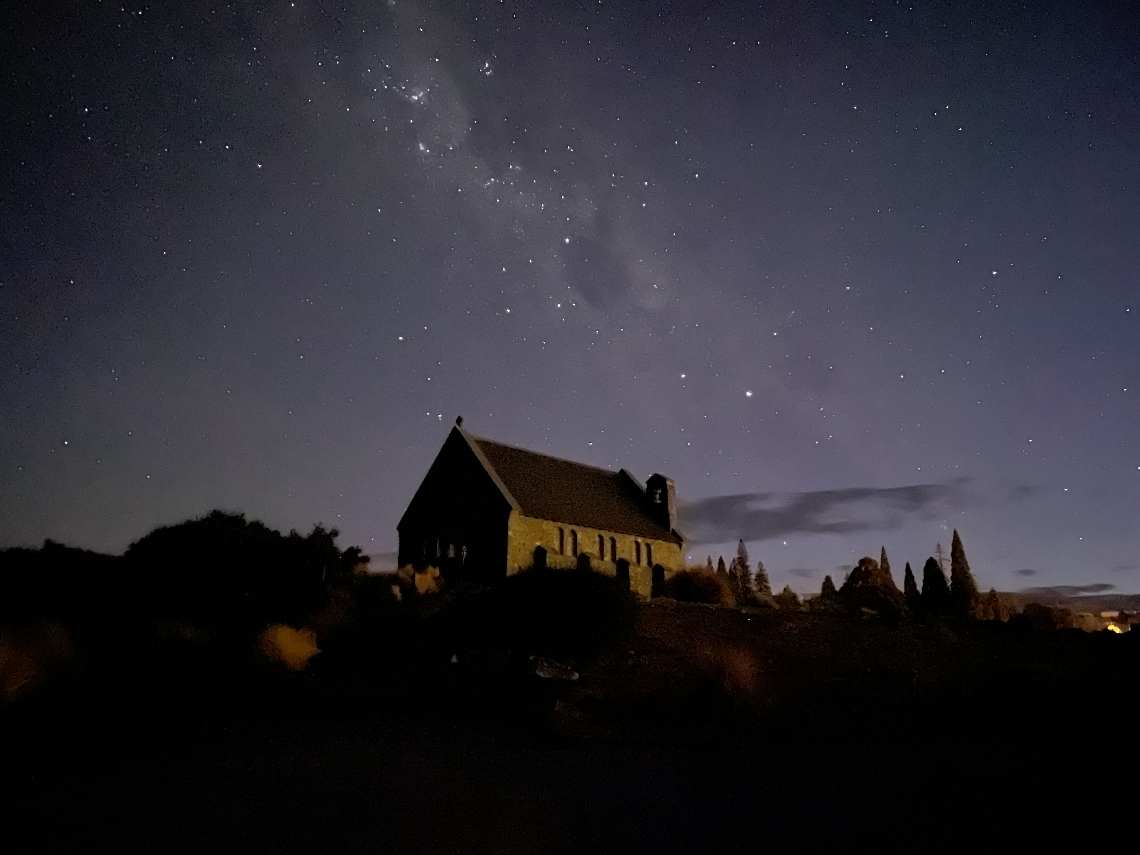 Silhouette di una piccola chiesa sotto un cielo stellato con vegetazione circostante