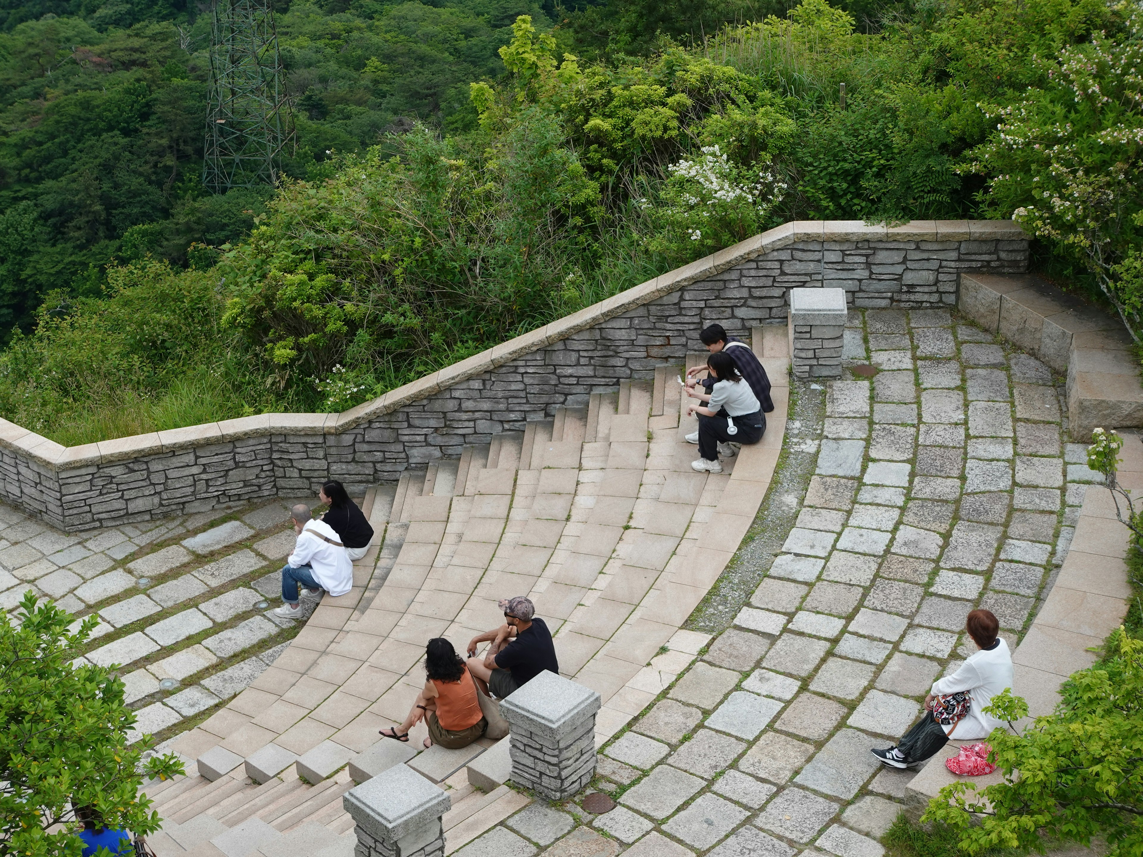 Des gens assis sur un escalier en pierre courbe entouré de verdure