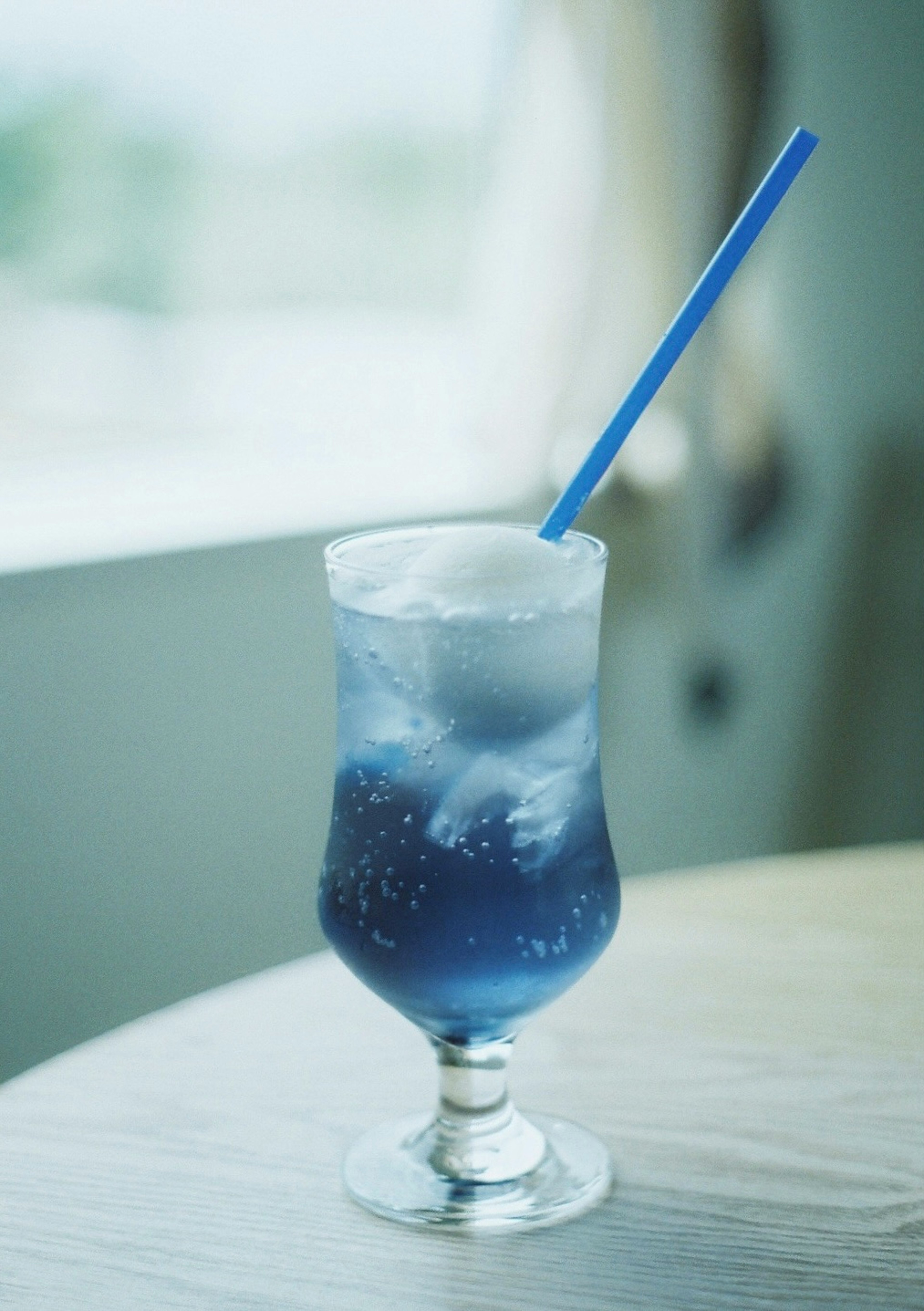 A glass of blue drink with ice and a blue straw