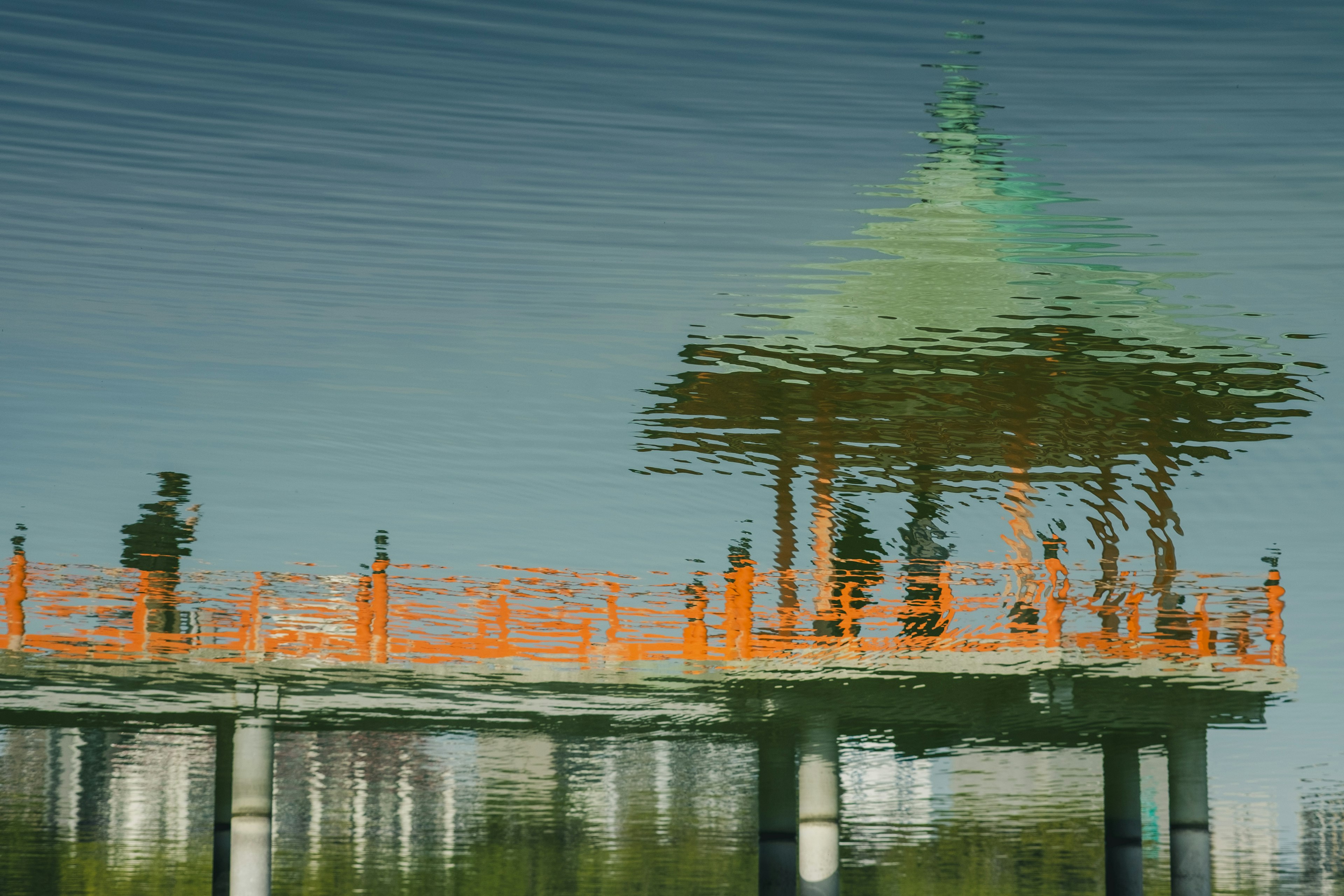 Reflection of an orange railing and green-roofed pavilion on water