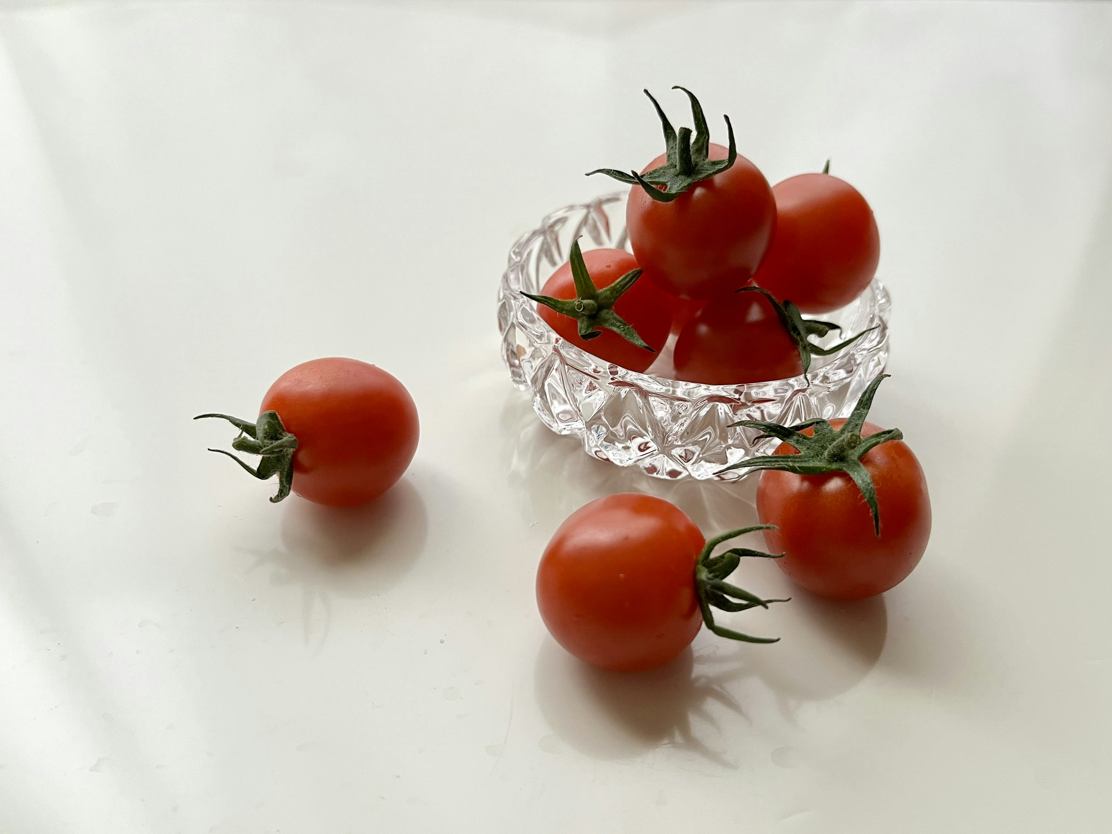 Pomodori freschi disposti in una ciotola di cristallo con pomodori aggiuntivi nelle vicinanze