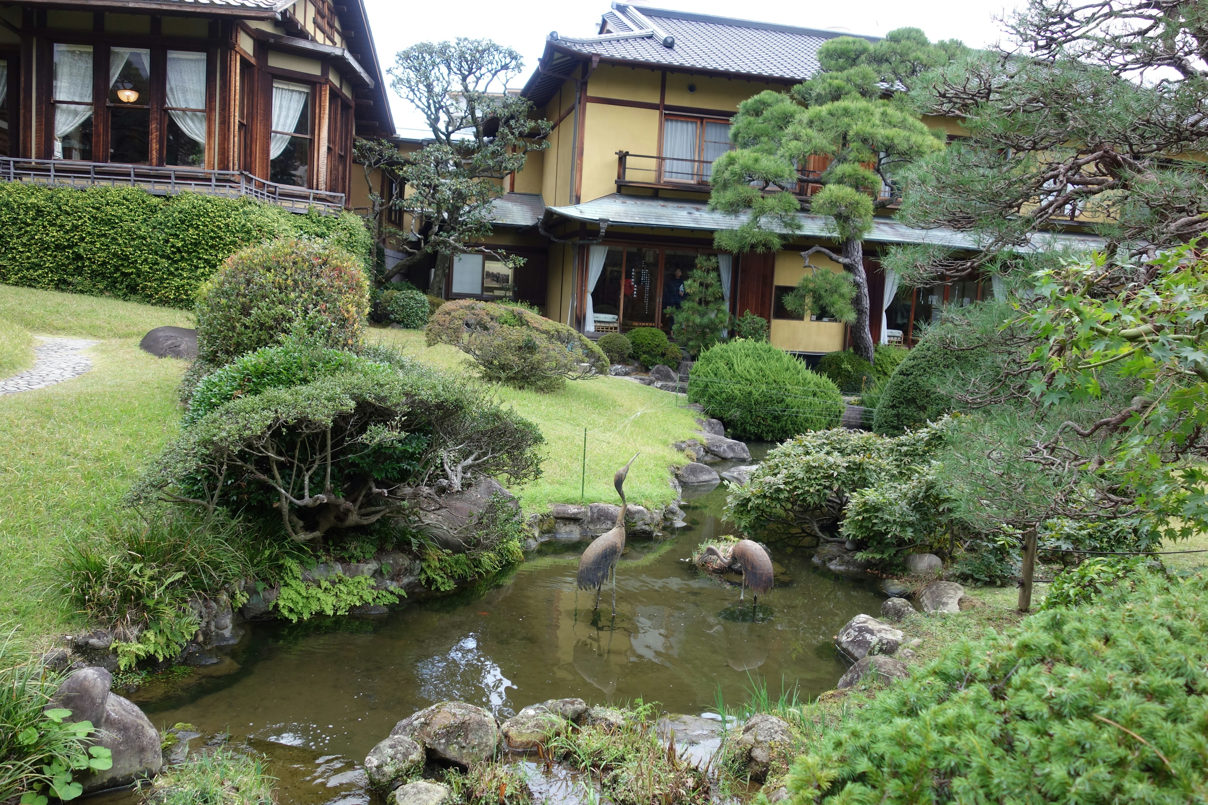 Rumah tradisional Jepang dikelilingi taman tenang dengan kolam dan vegetasi subur