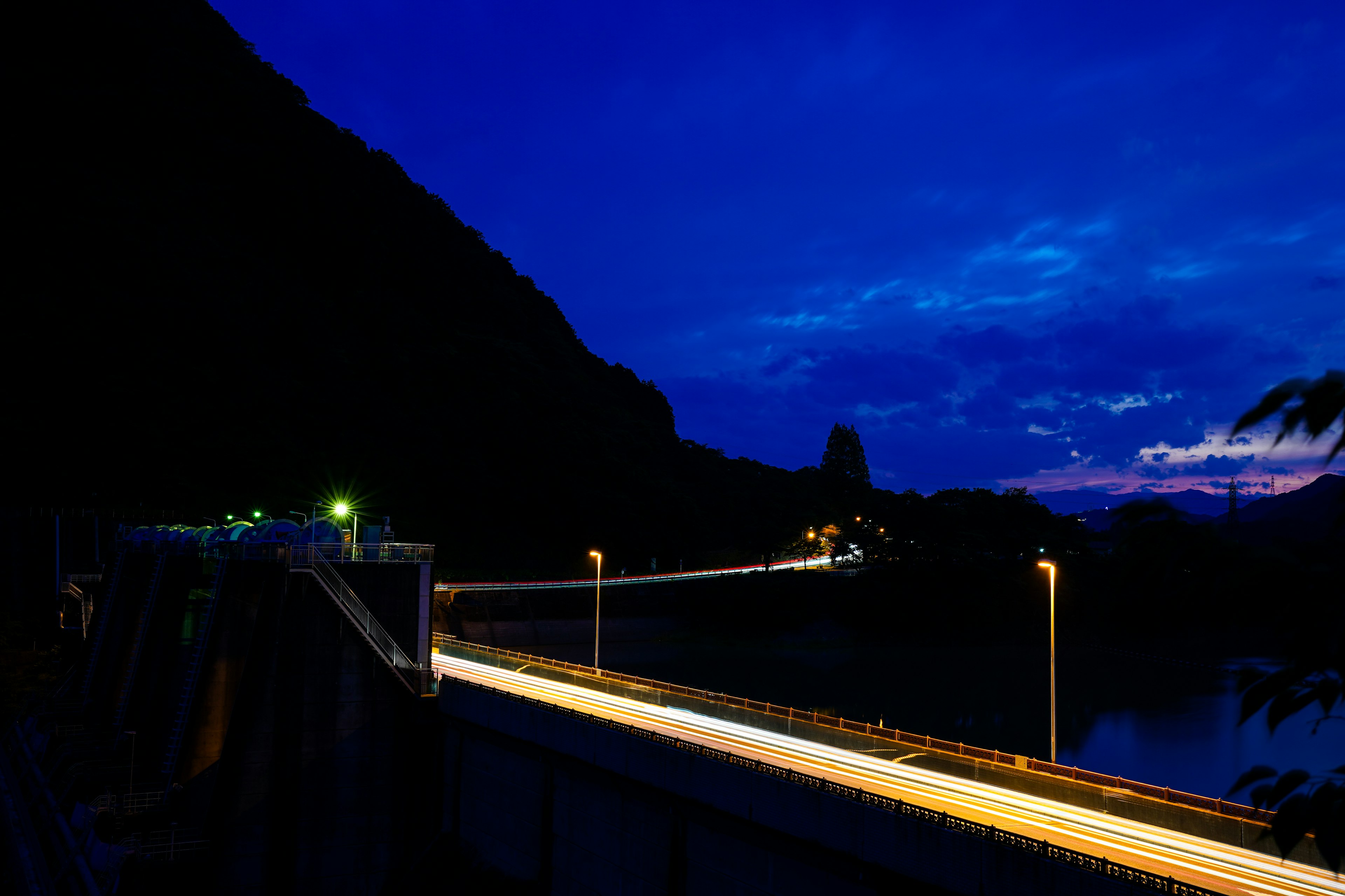 Vista nocturna de un puente con cielo azul y luces de coches en movimiento