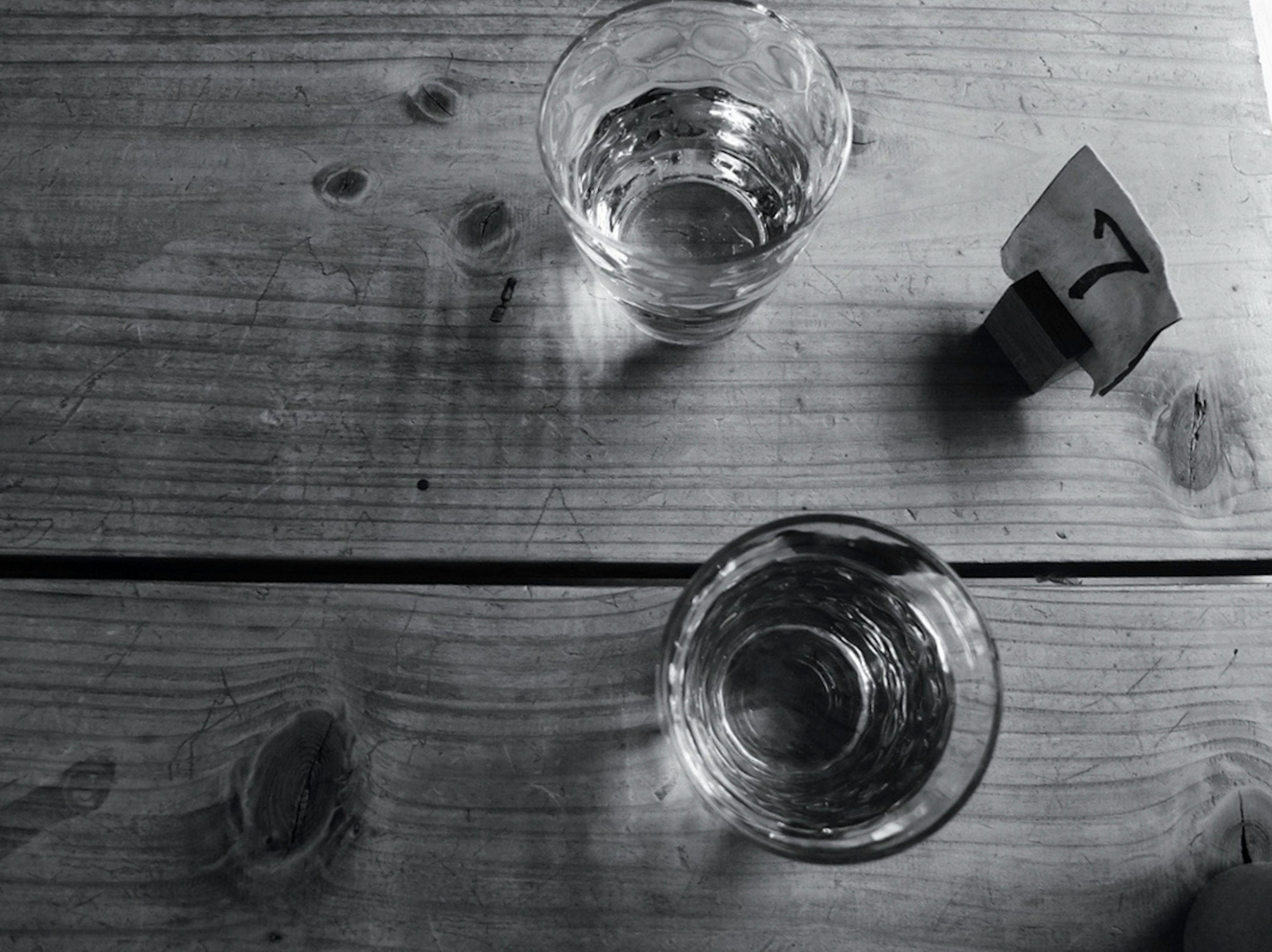 Two clear glasses filled with water on a wooden table with a numbered tag