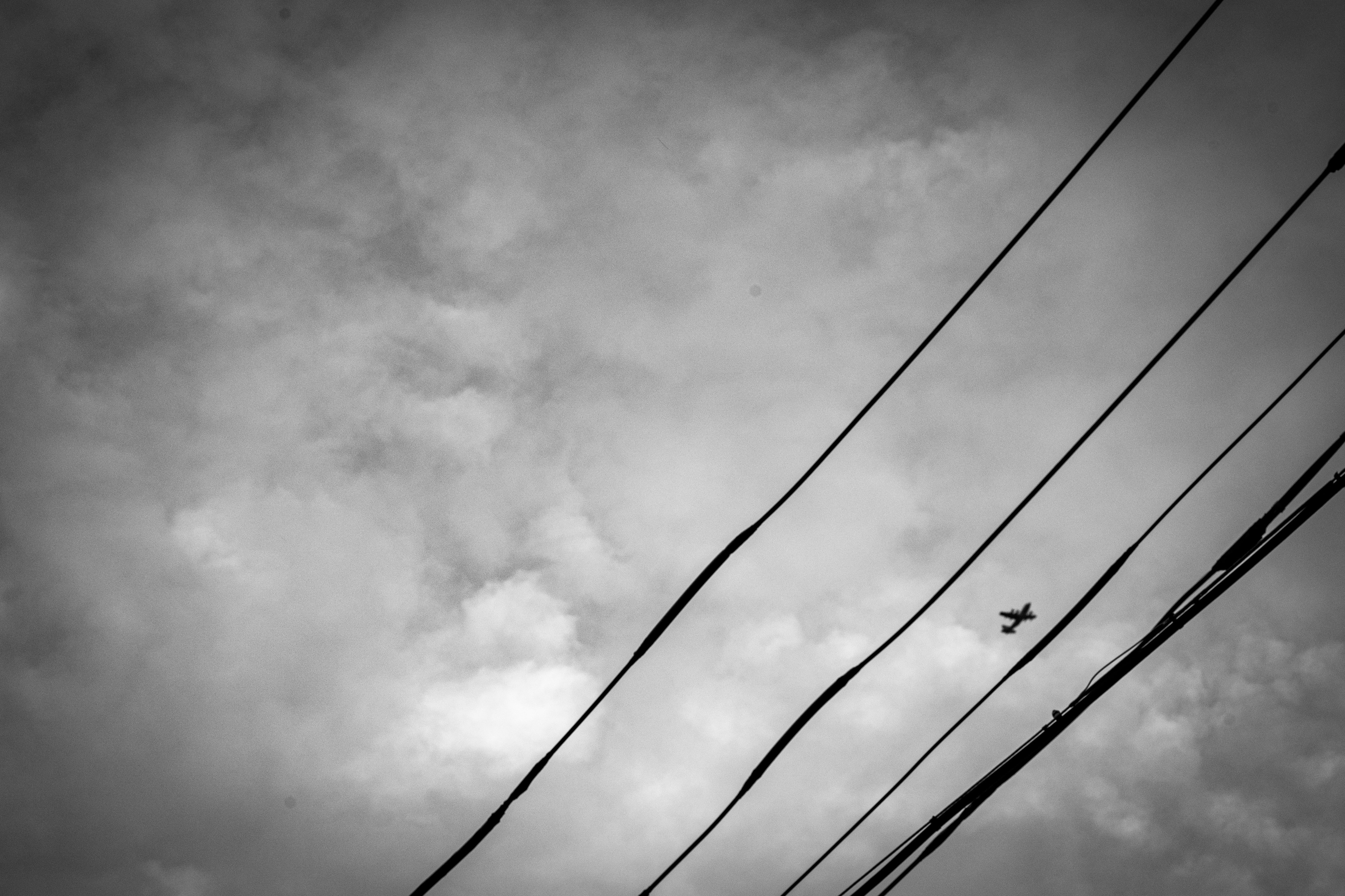 Silhouette eines kleinen Flugzeugs, das gegen einen bewölkten Himmel mit Stromleitungen fliegt