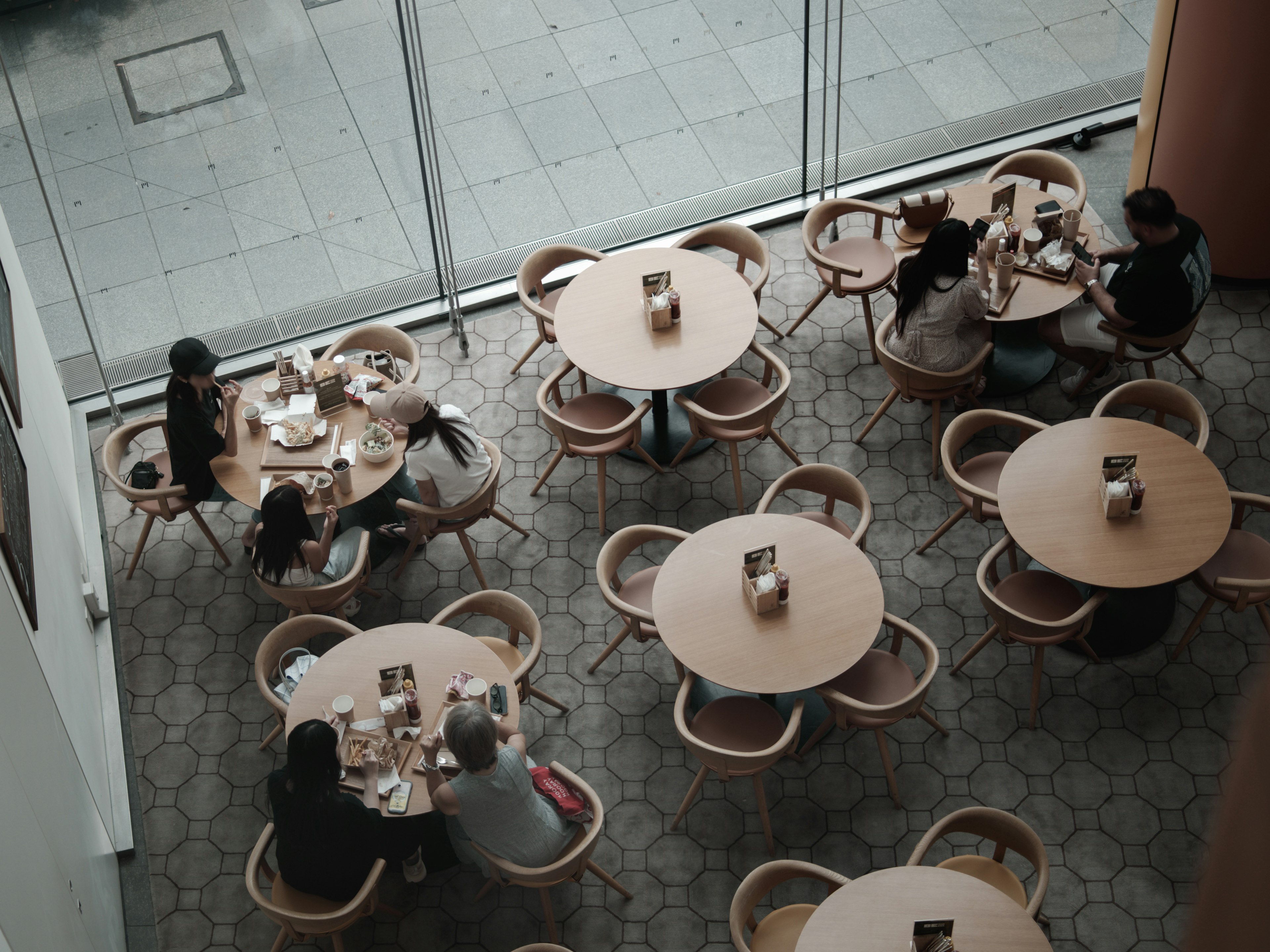 Interior de un café con mesas redondas y sillas donde los clientes disfrutan de sus comidas