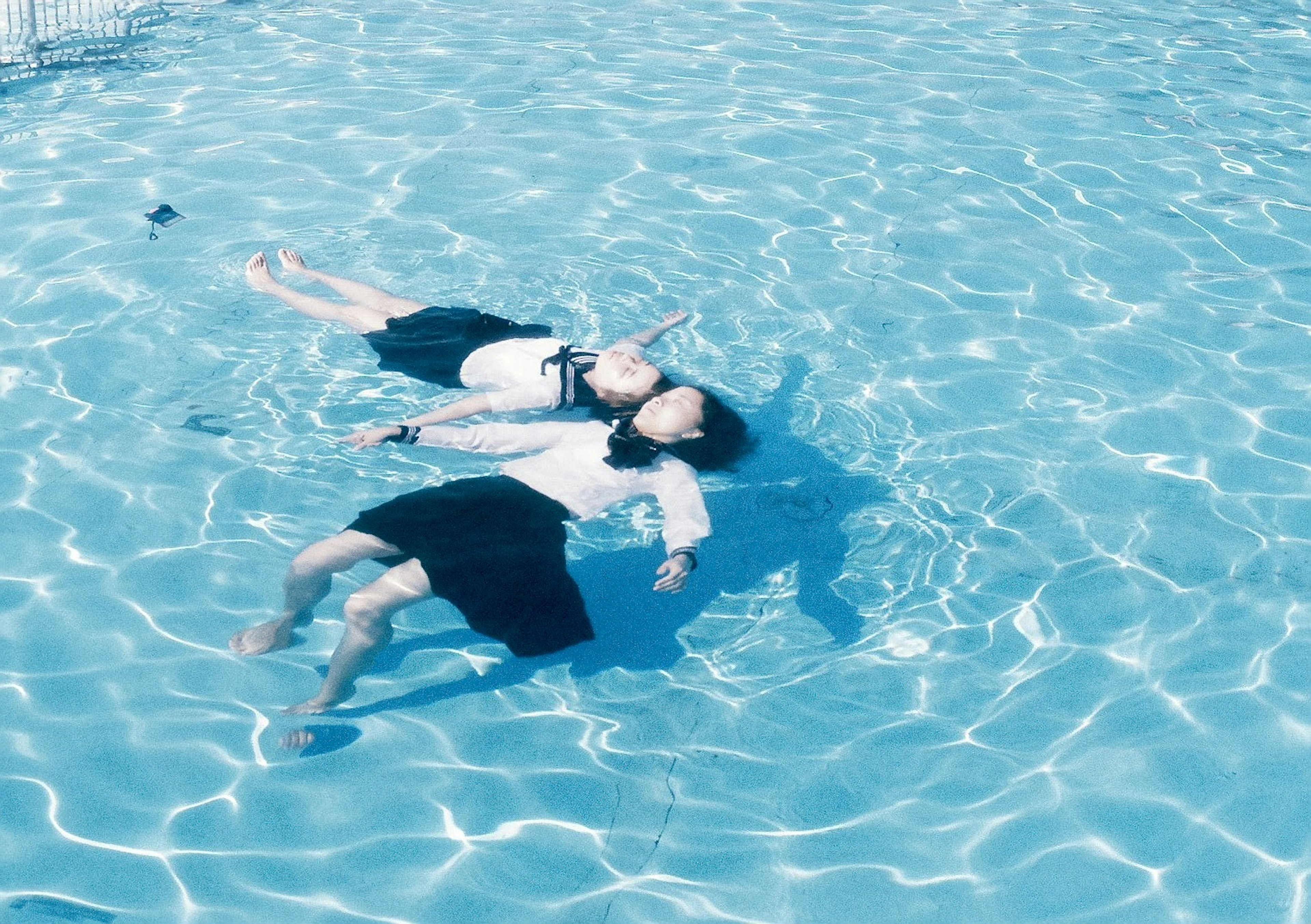 Zwei Figuren, die auf einer blauen Wasseroberfläche mit Lichtreflexionen schwimmen