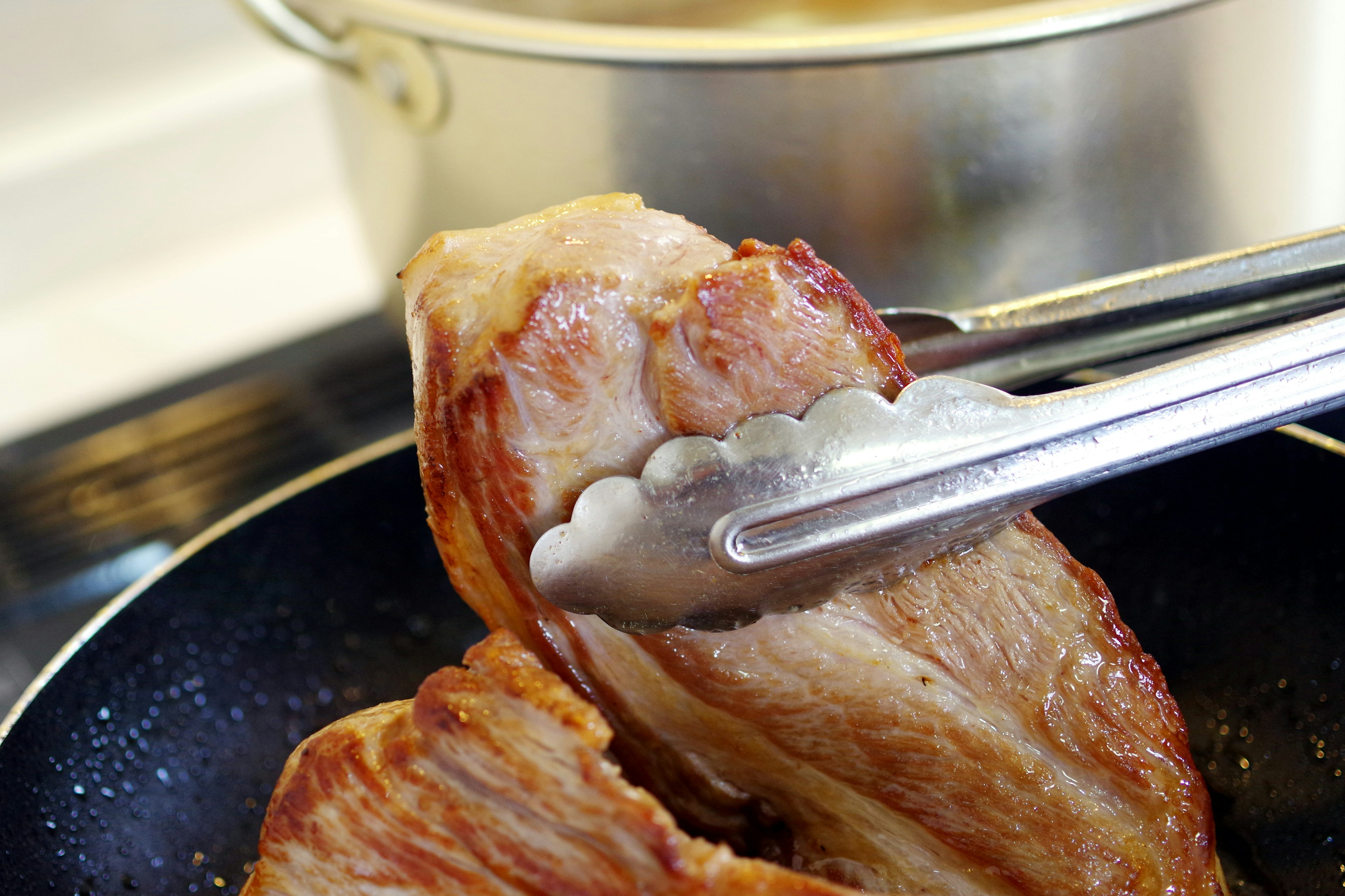 A piece of meat being lifted with tongs from a frying pan