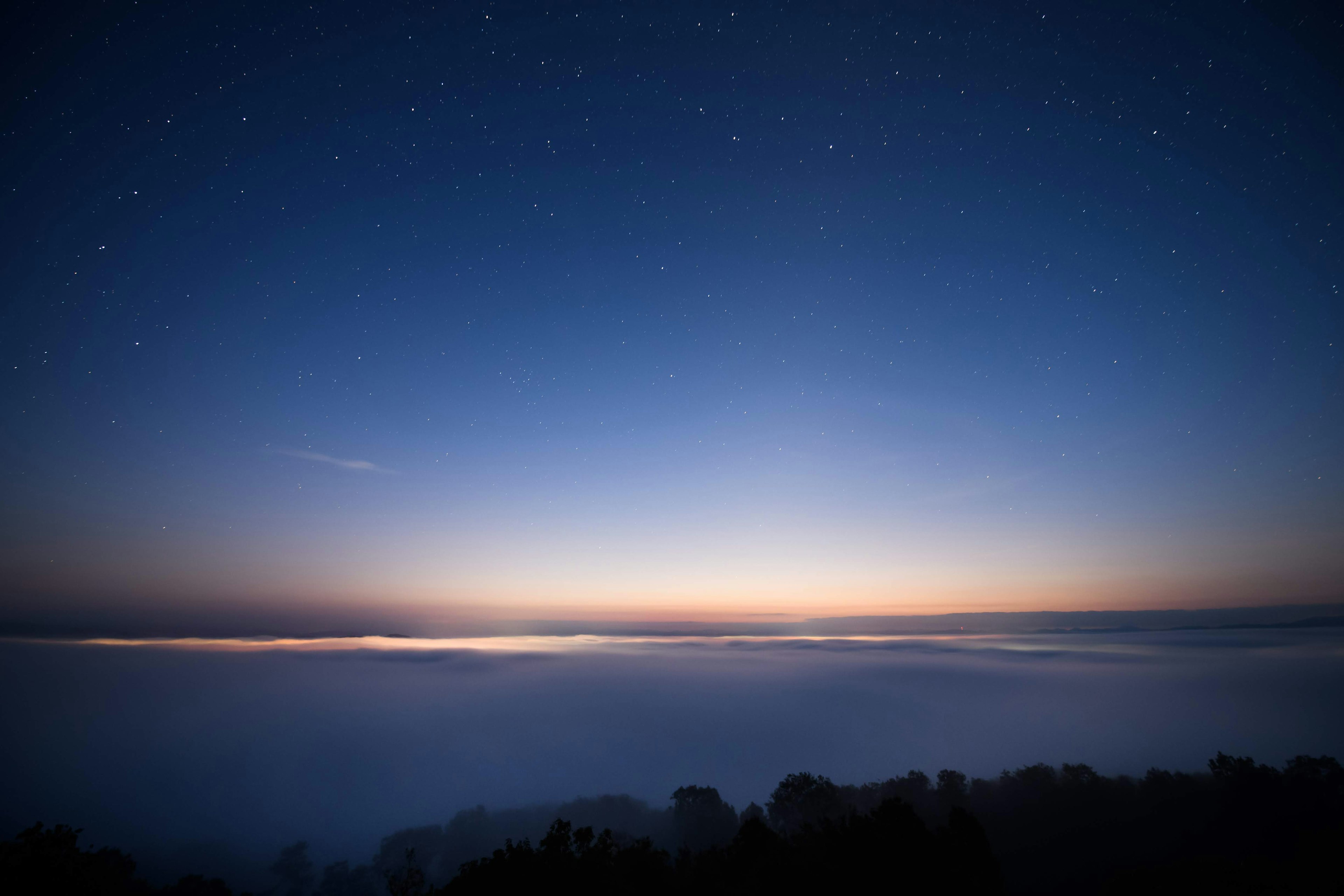 Hermoso amanecer sobre un mar de nubes con un cielo nocturno azul y estrellas