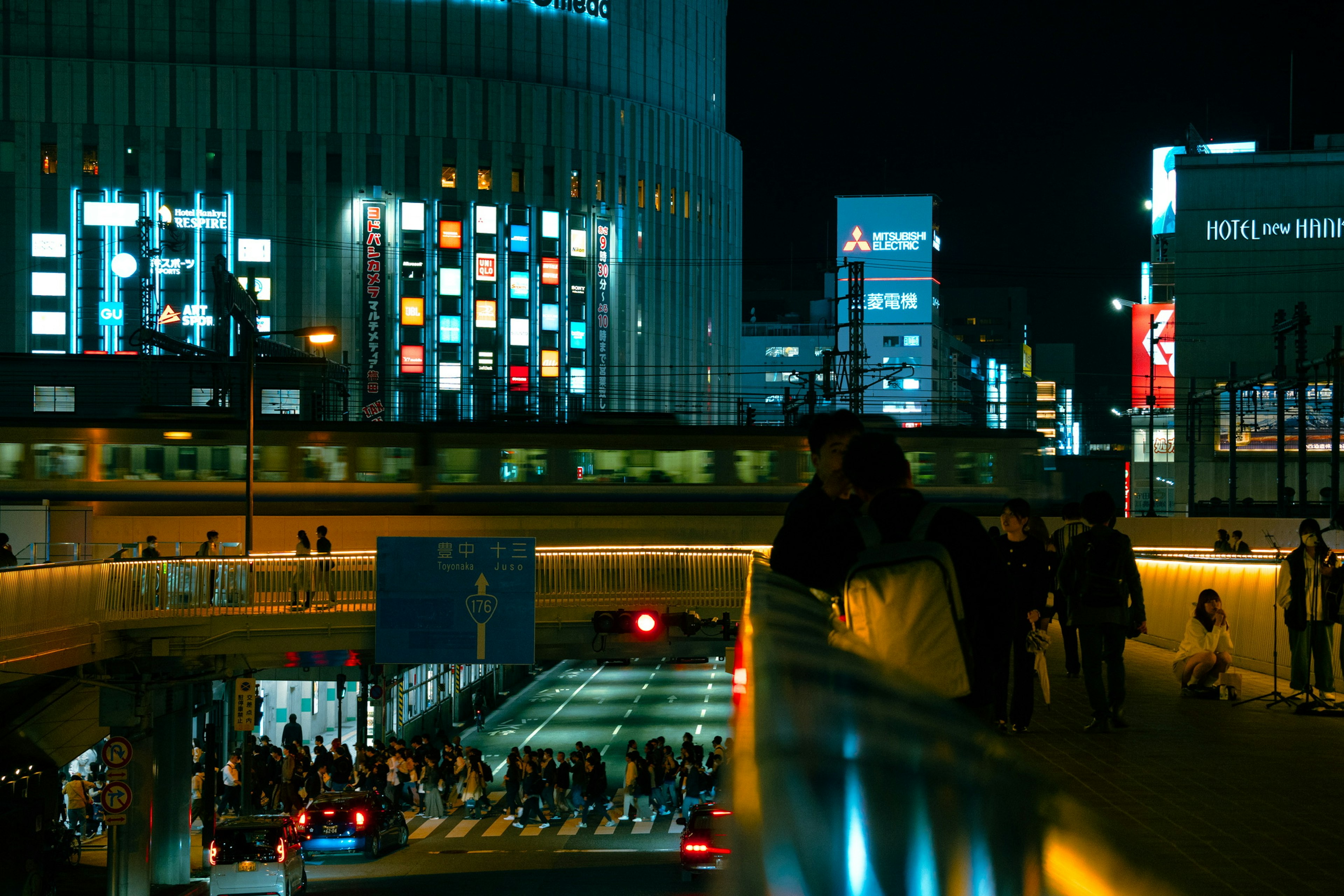 Scène urbaine nocturne avec des personnes marchant sur un passage piéton et des bâtiments illuminés