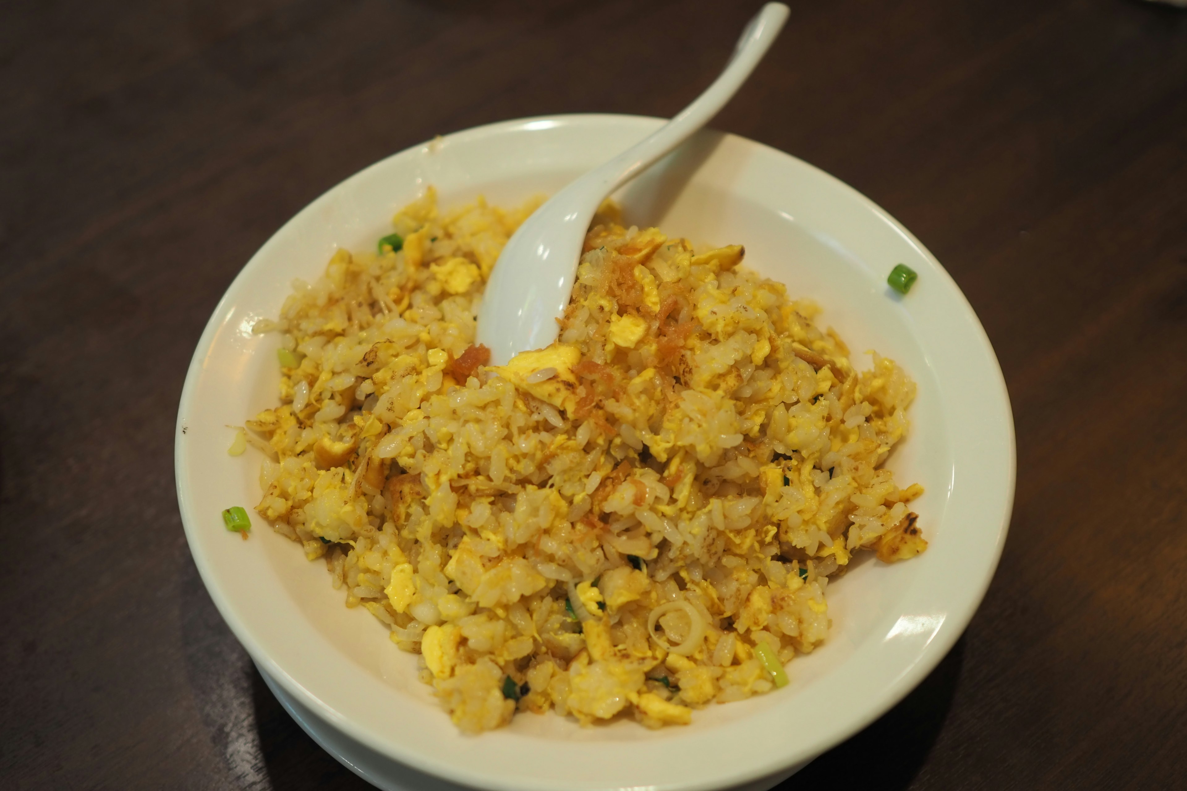 Arroz frito servido en un tazón blanco con huevo y guisantes verdes