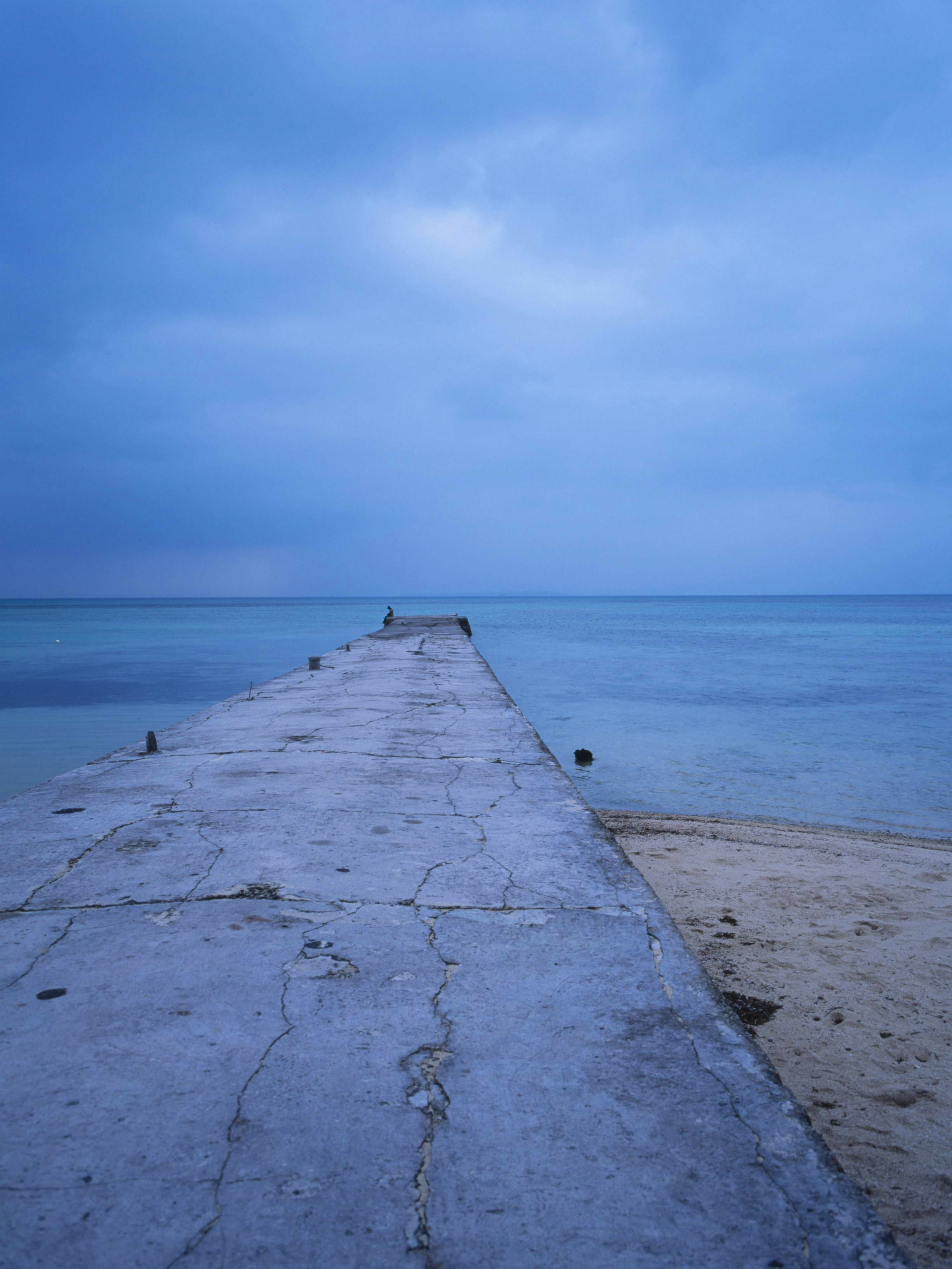 Quai en béton s'étendant dans la mer bleue sous un ciel nuageux