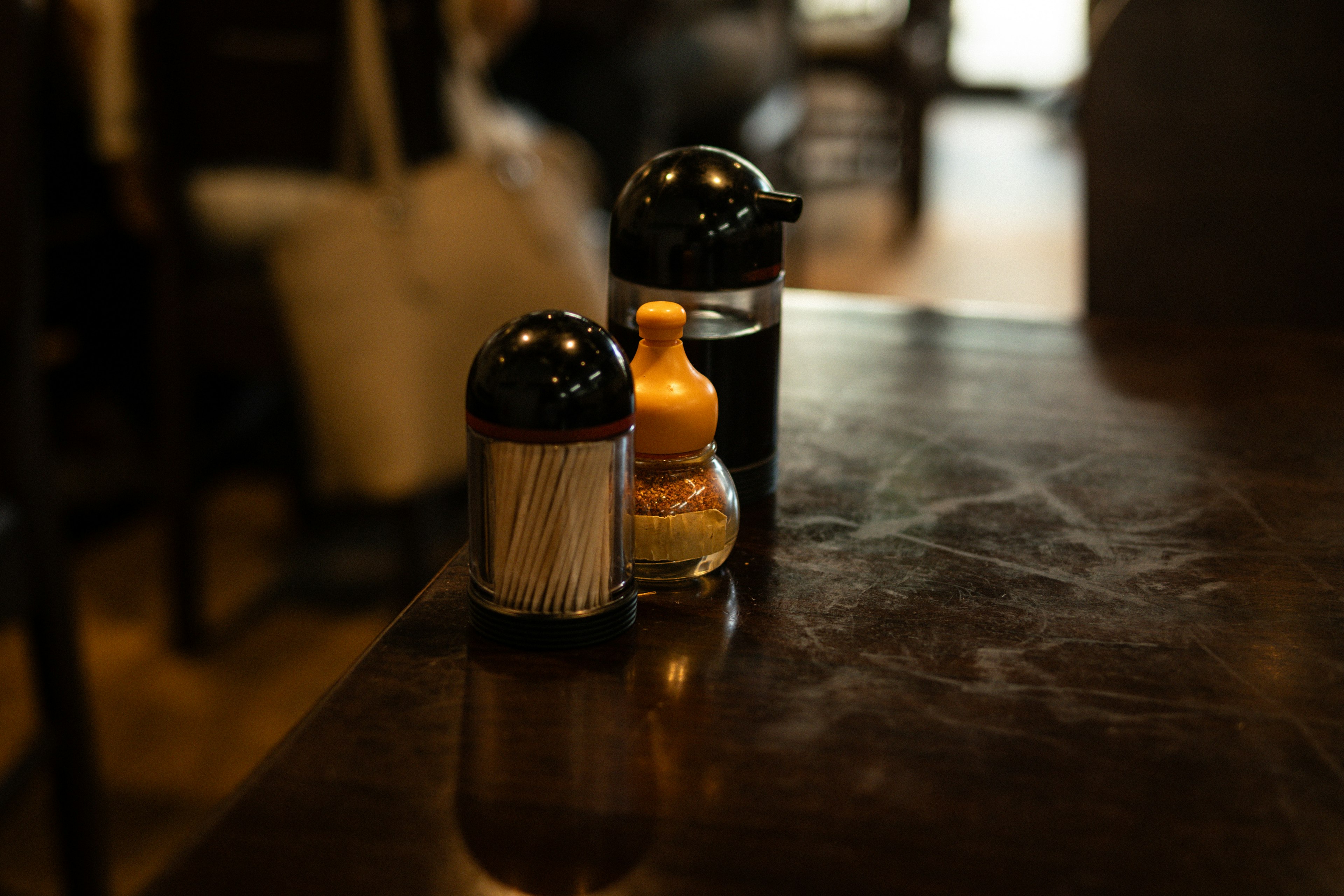 Condiment containers on a wooden table with a black cap and a yellow bottle