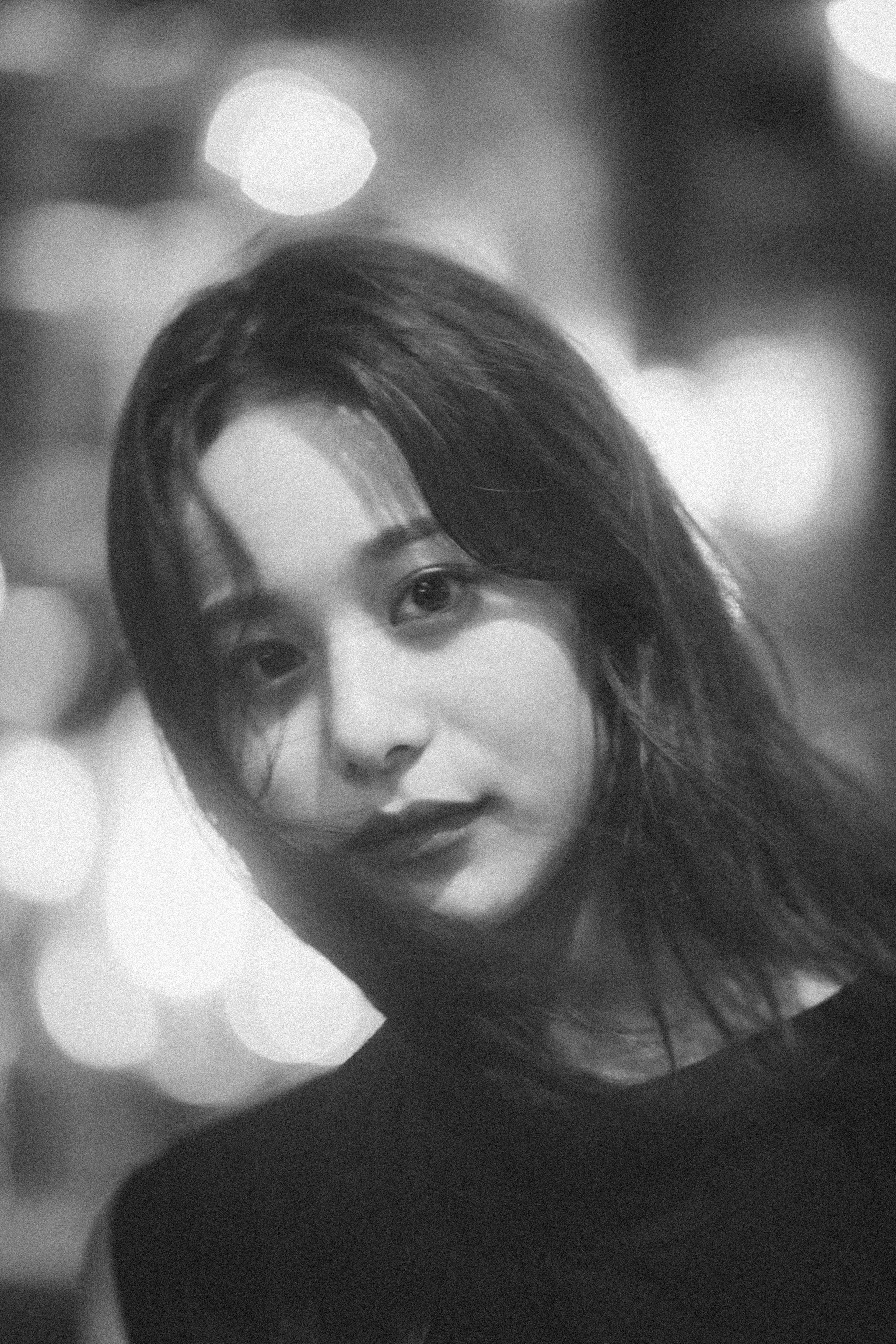 Black and white portrait of a woman with a soft bokeh background showing a gentle smile