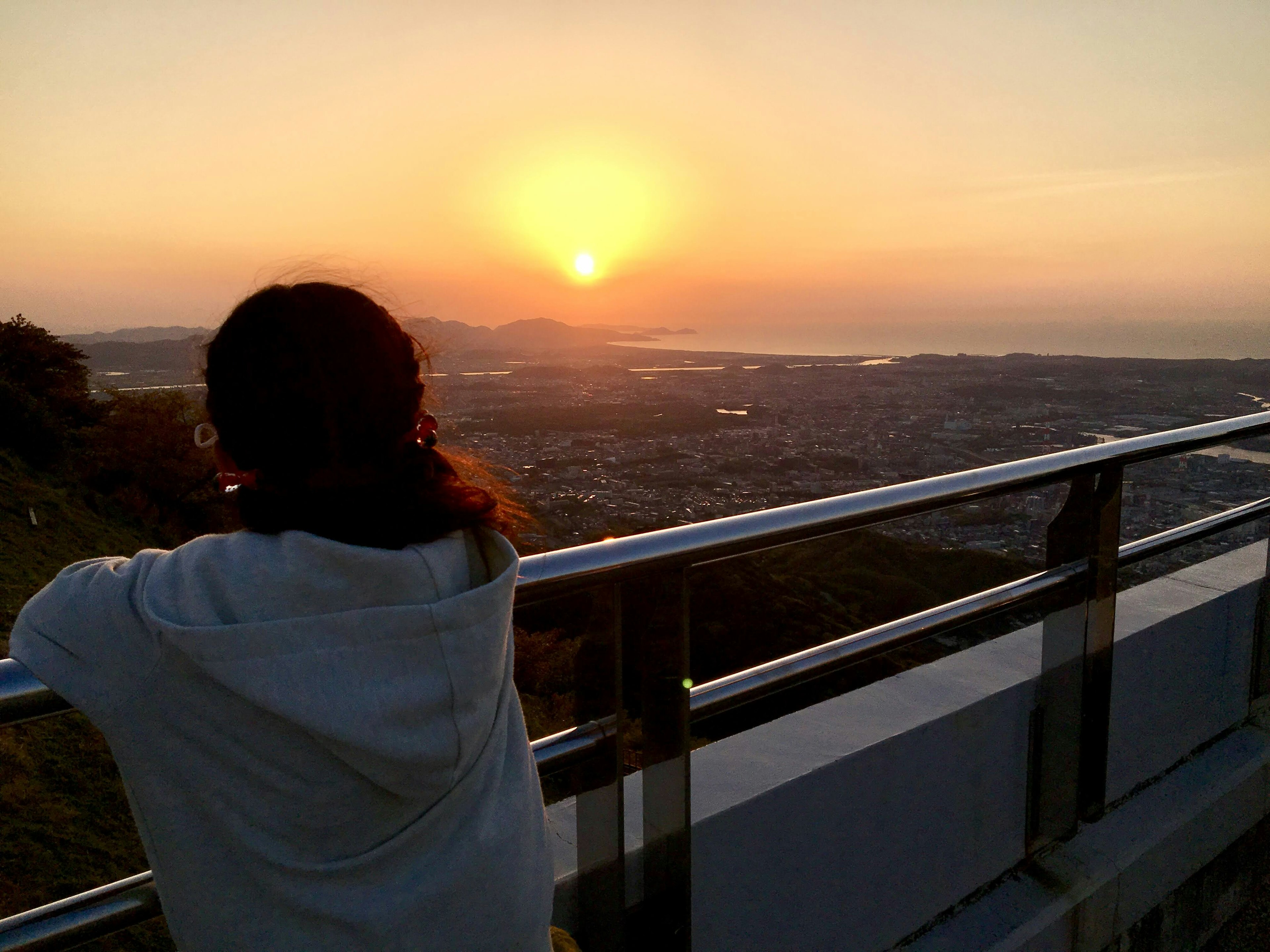 Silhouette einer Frau, die den Sonnenuntergang über einer Landschaft beobachtet