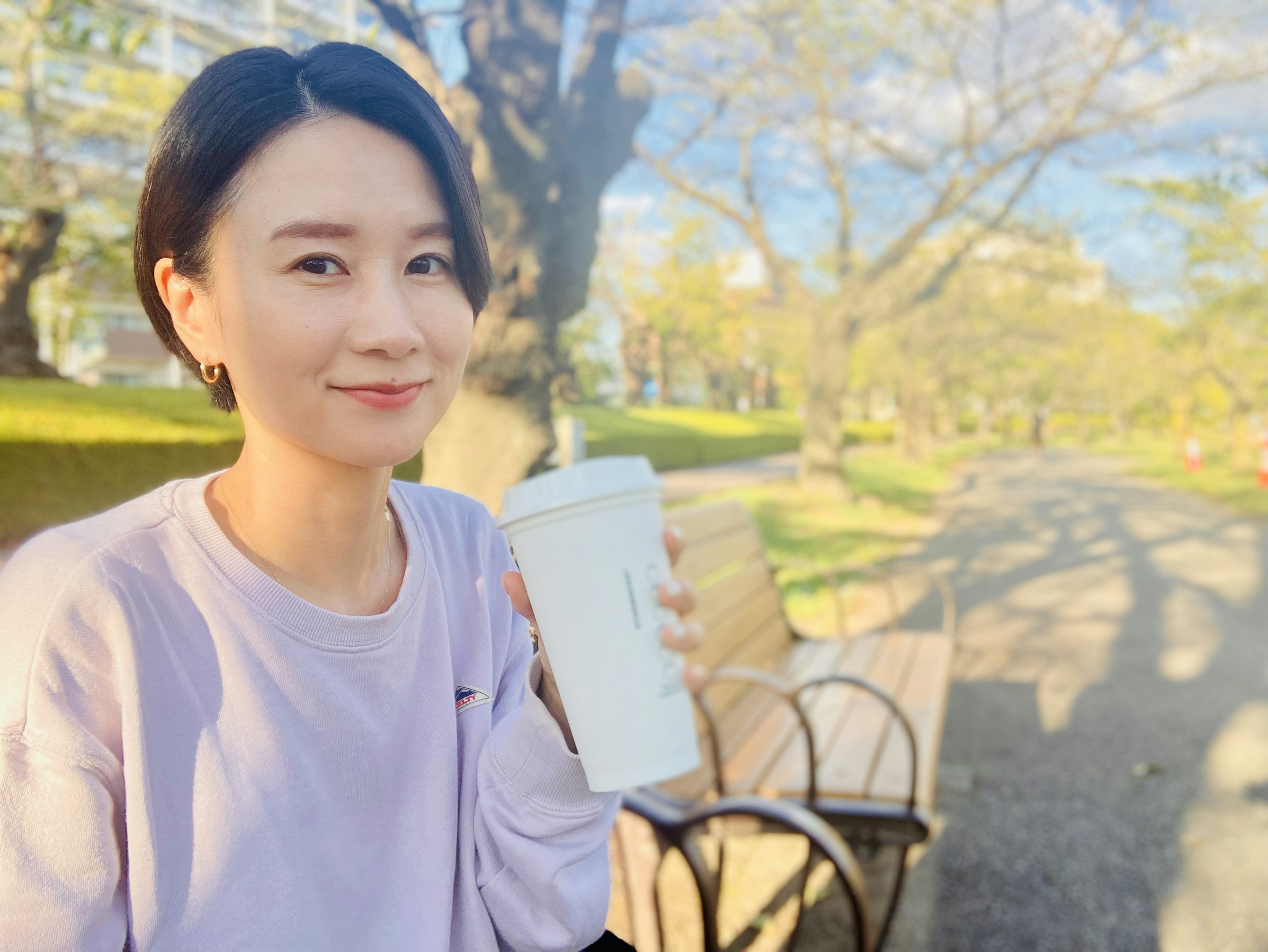 Mujer sonriente sosteniendo una taza blanca en un parque