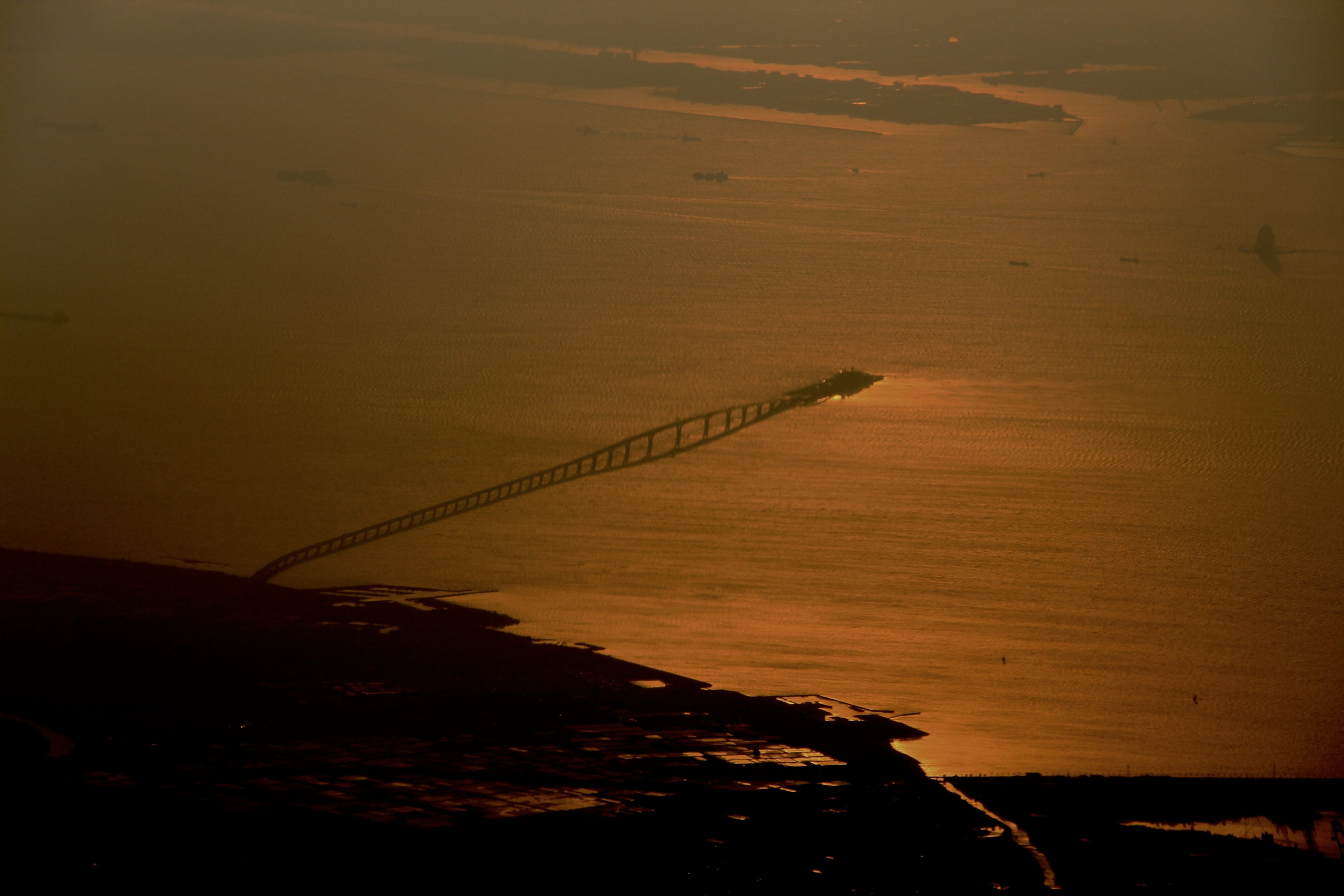 Vista aérea de un puente al atardecer con reflejos naranjas en el agua