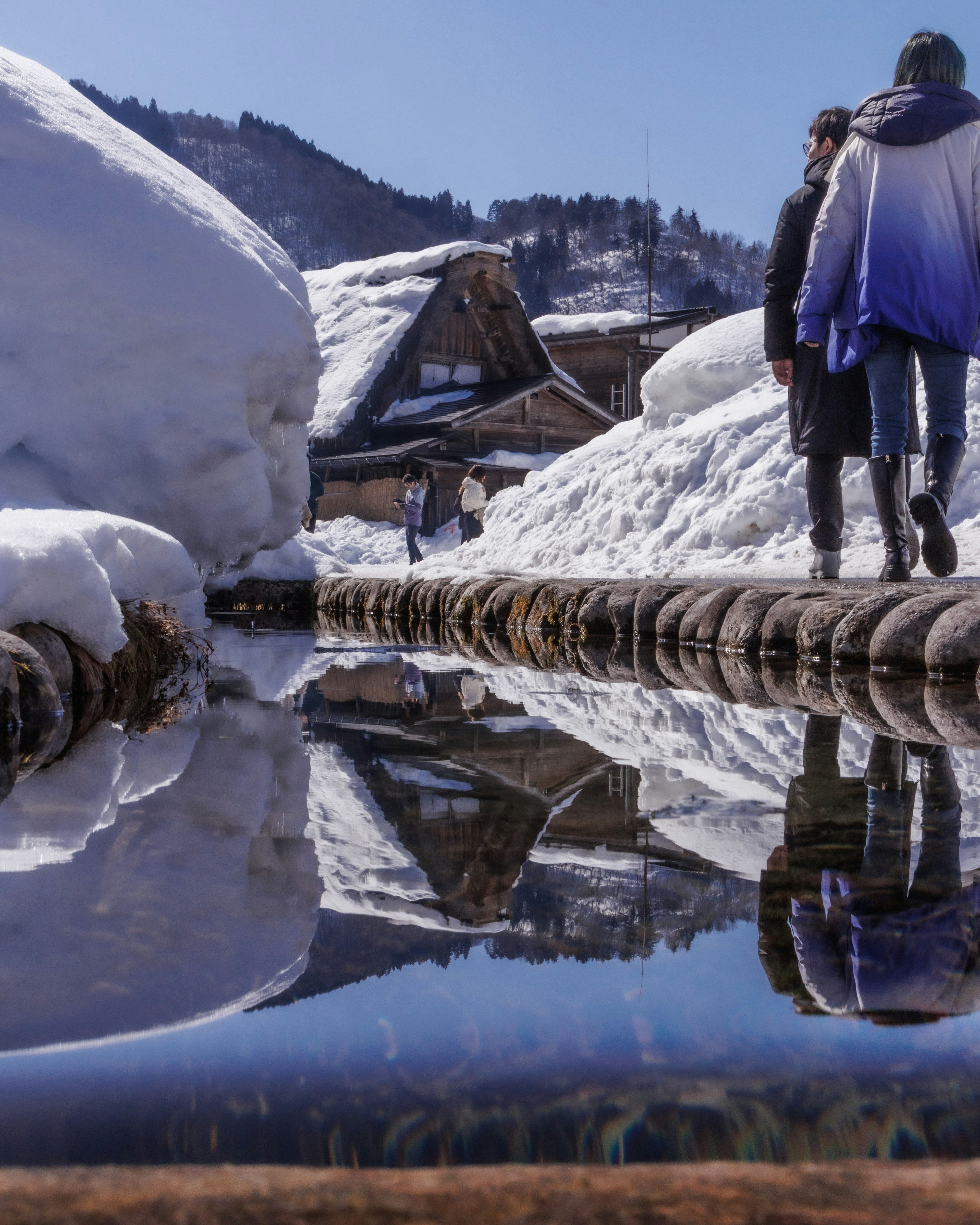 Snow-covered landscape with reflections of houses and people in water