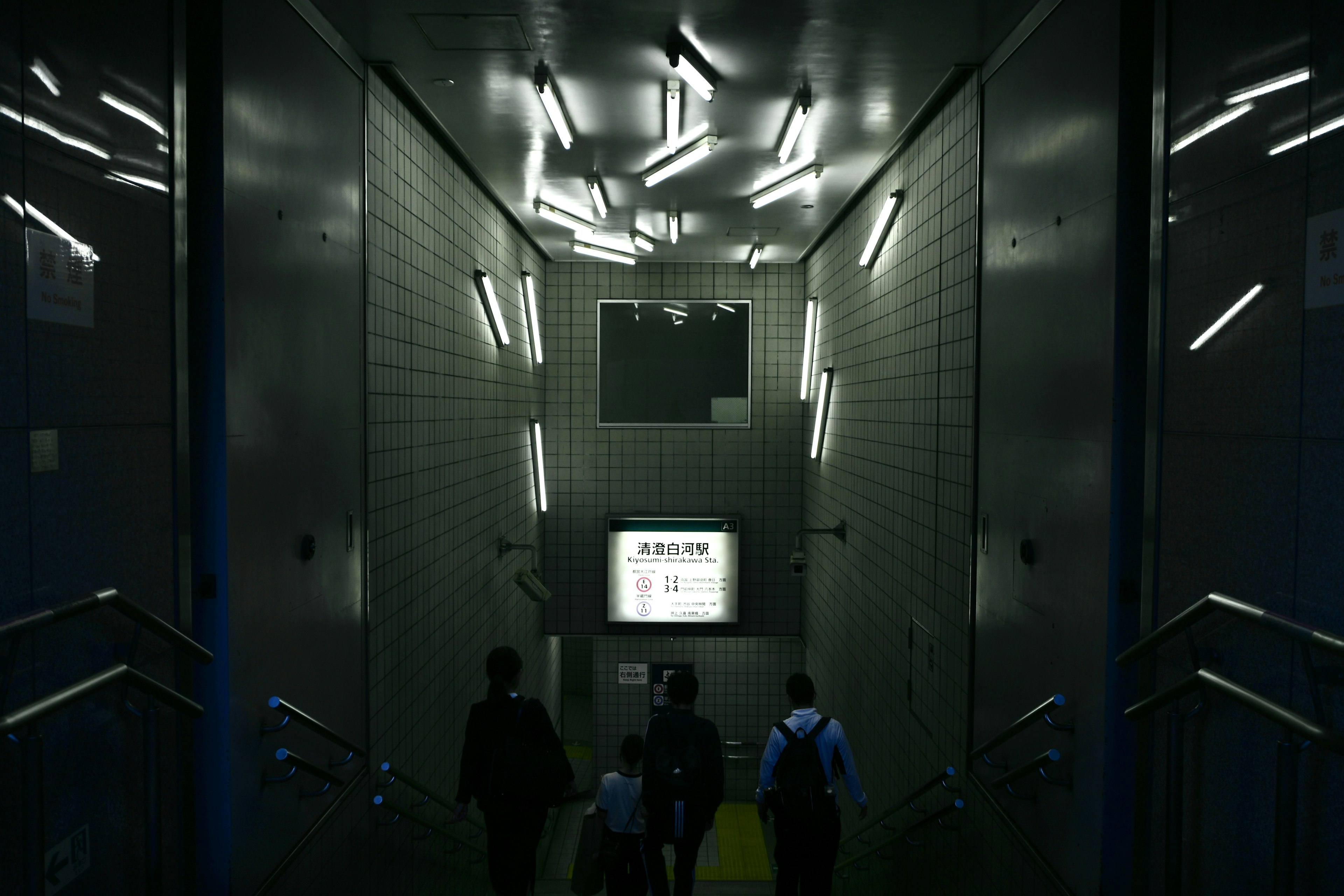 Personas caminando por un pasillo oscuro con luces fluorescentes brillantes en las paredes