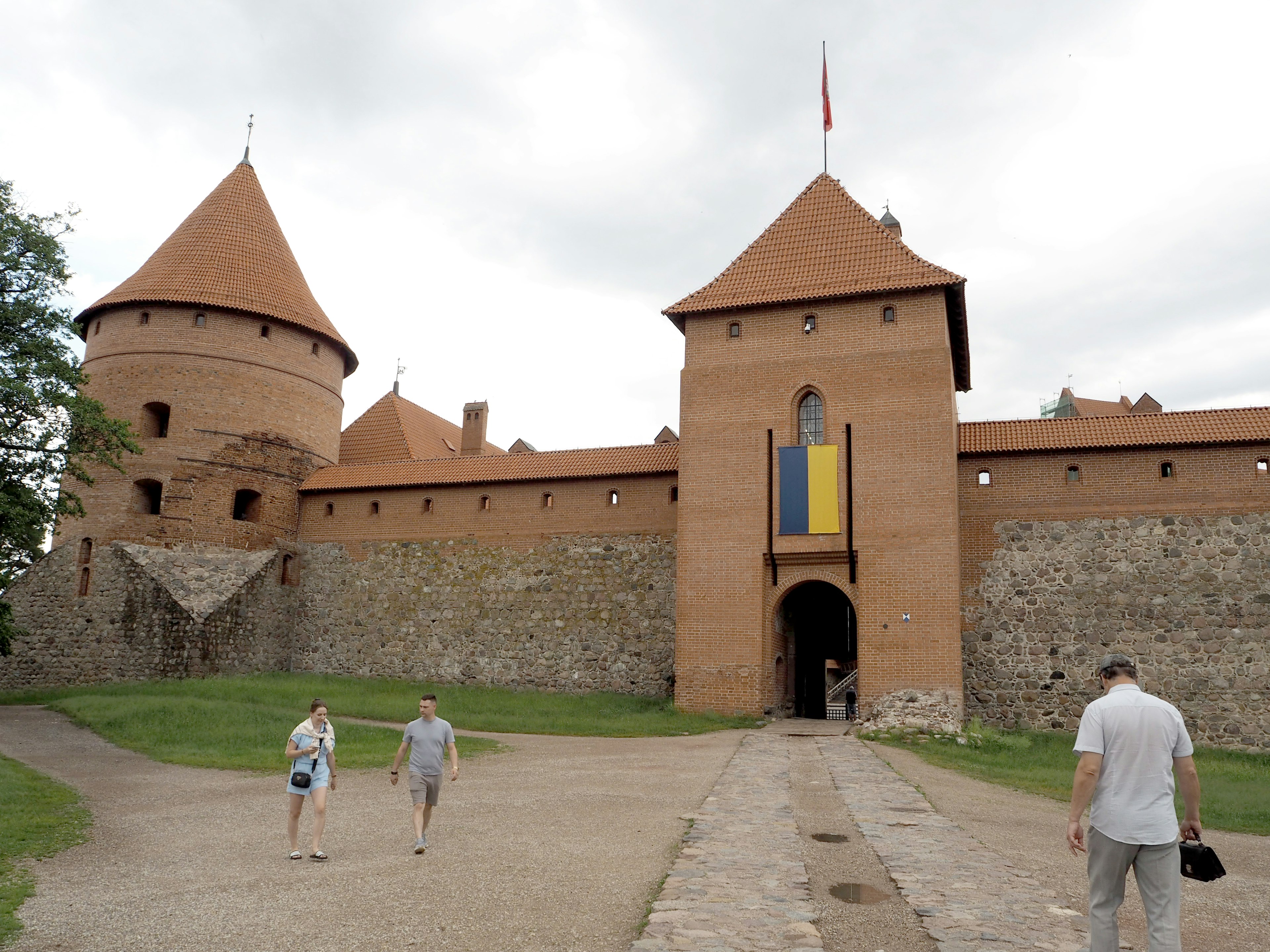 Entrance of a castle with orange roofs and people walking near it featuring the Ukrainian flag