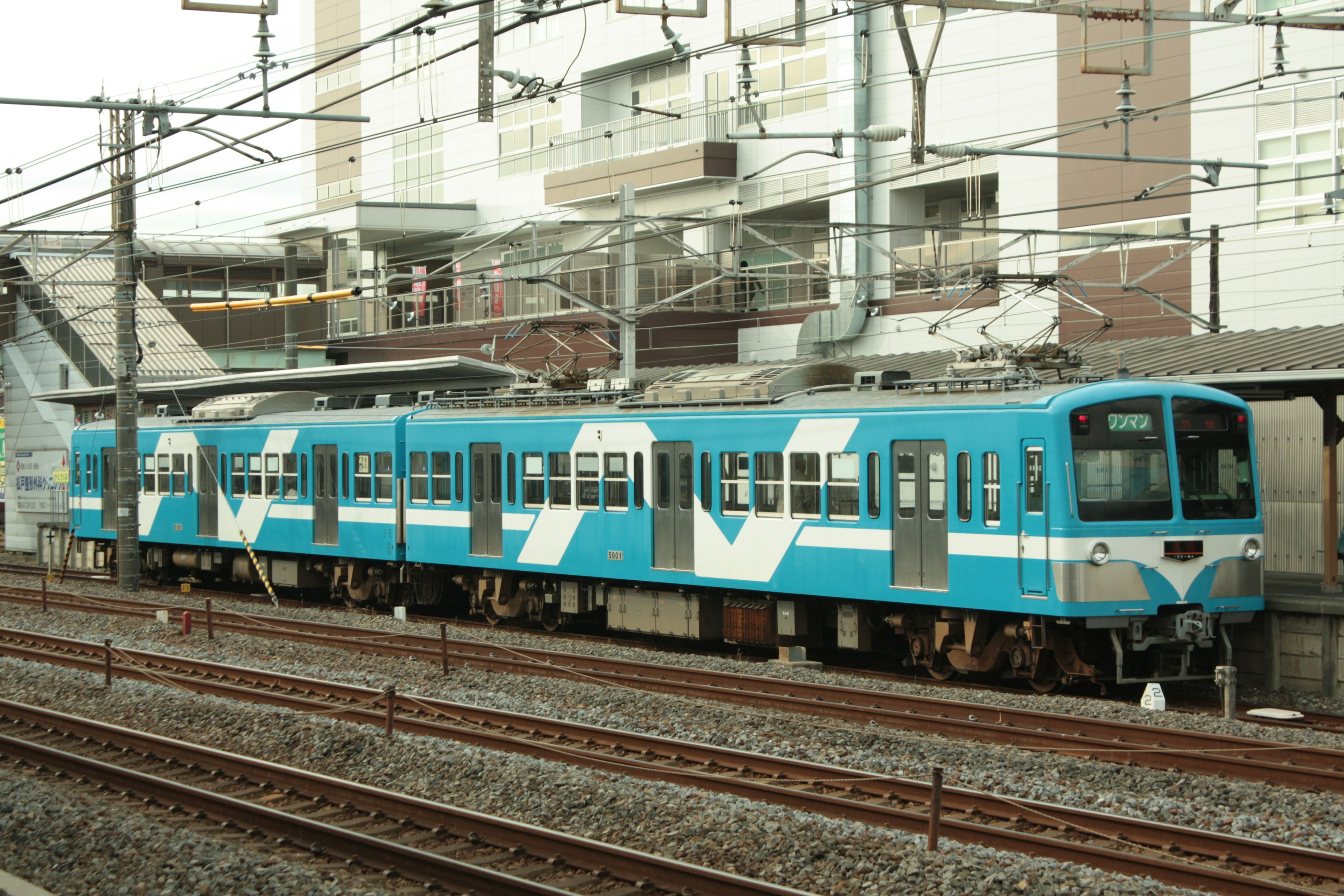 Ein blauer Zug an einem Bahnhof mit sichtbaren Gleisen und Gebäuden