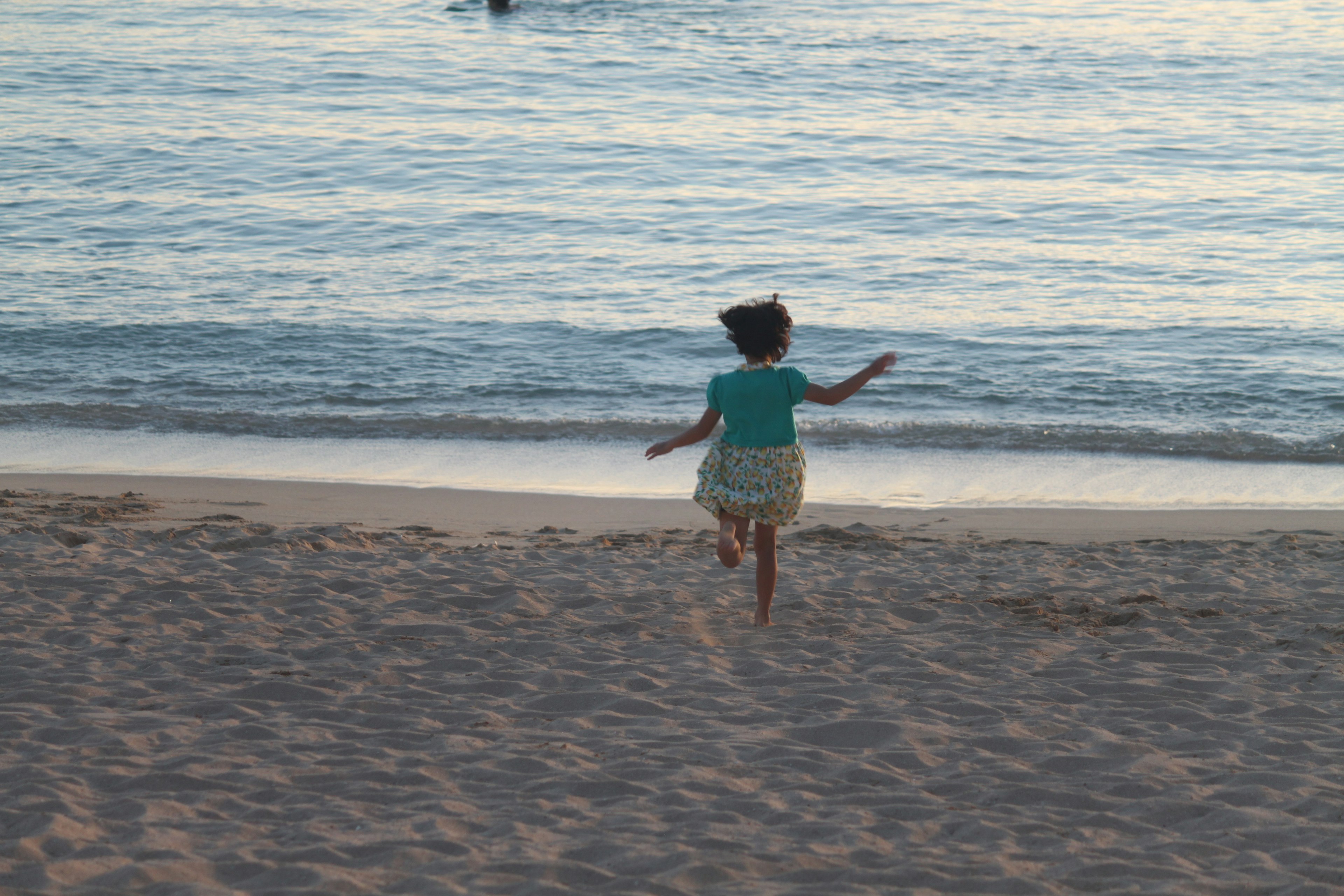 Kind, das am Strand läuft und zum Meer blickt