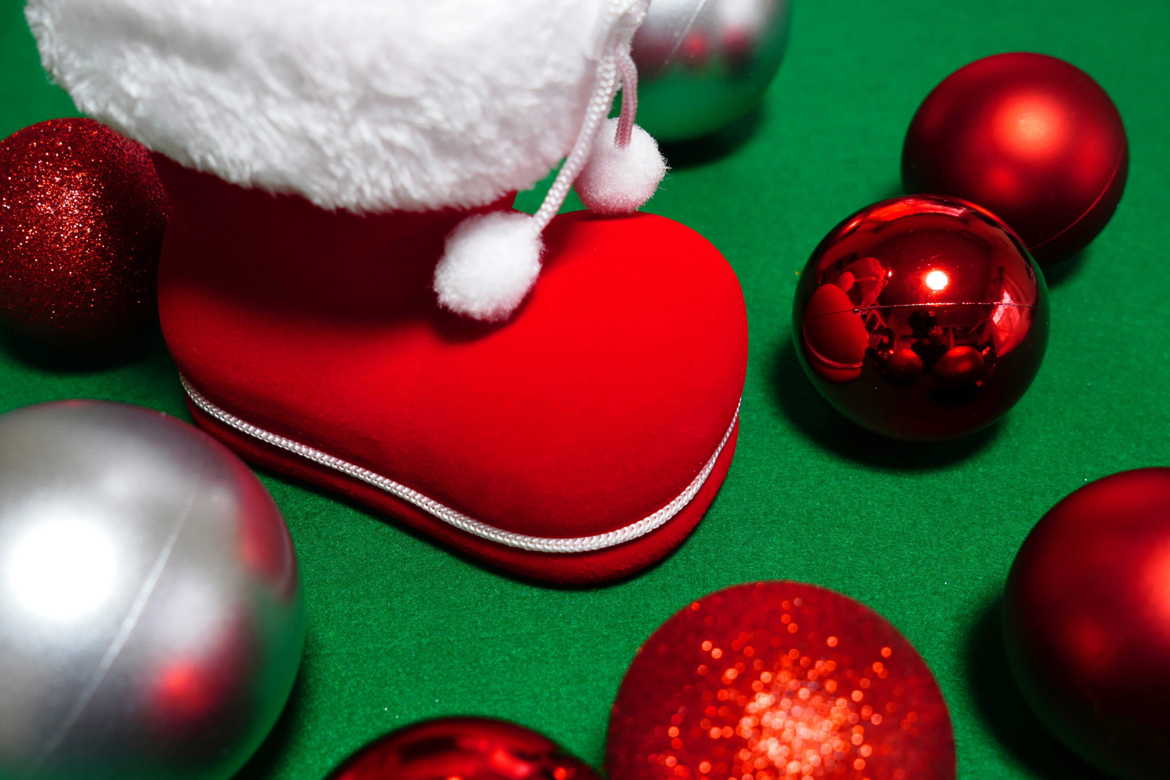 Rote Weihnachtsstiefel von Santa umgeben von roten und silbernen Weihnachtsornamenten auf grünem Hintergrund