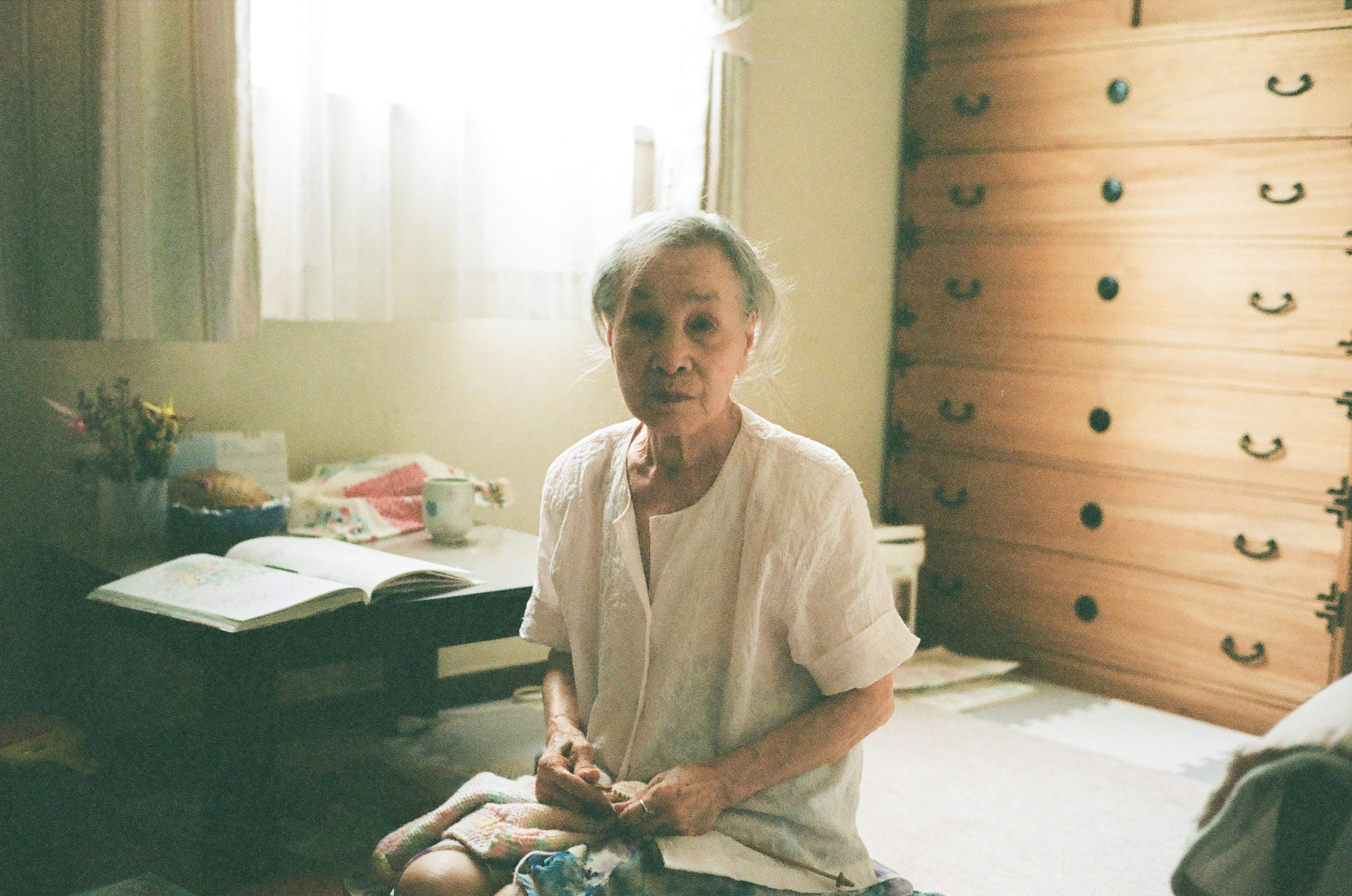 Mujer anciana sentada en una habitación Espacio brillante con luz natural Expresión tranquila y ropa sencilla