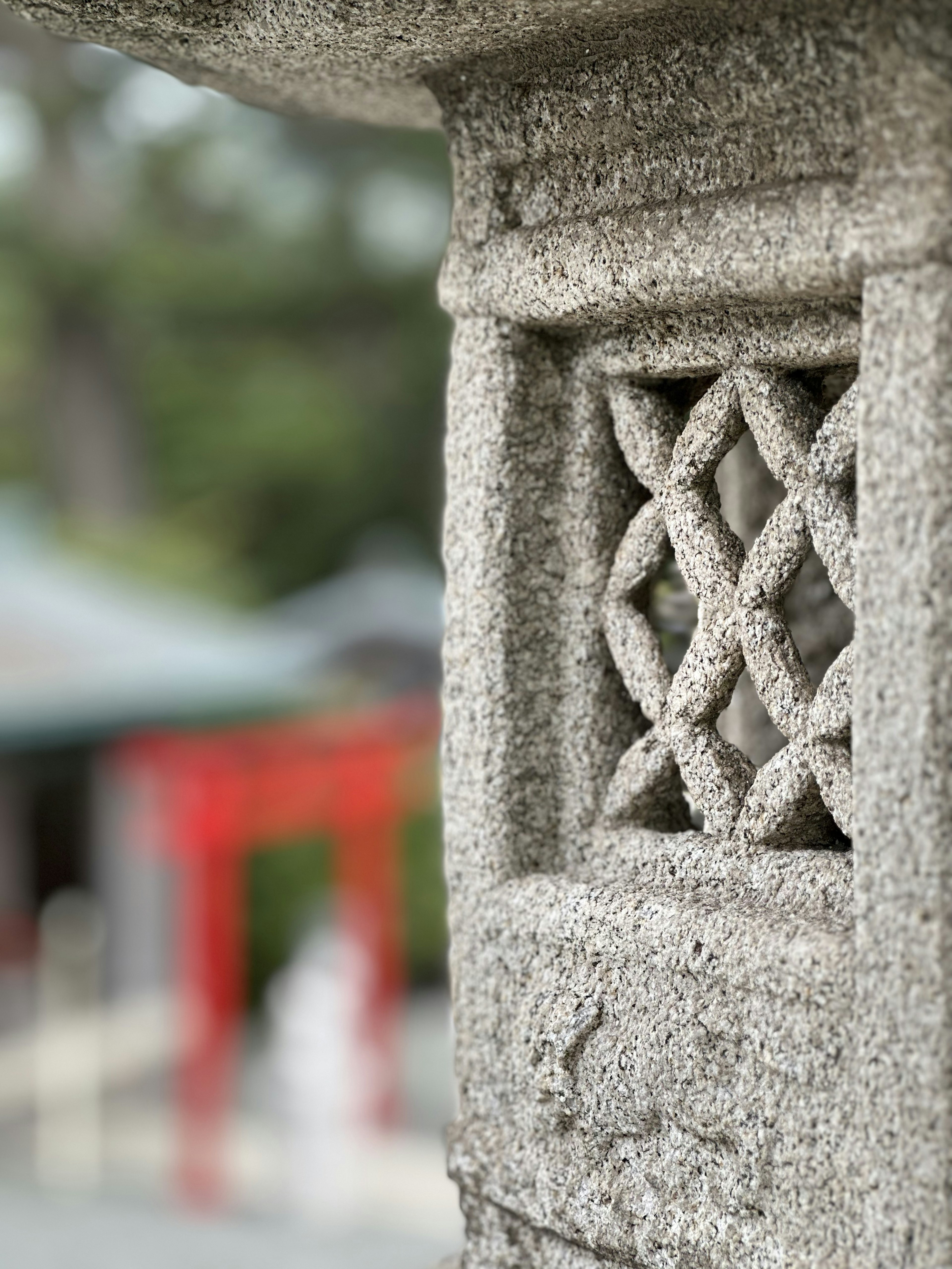 Ukiran halus pada lentera batu dengan gerbang torii merah yang kabur di latar belakang