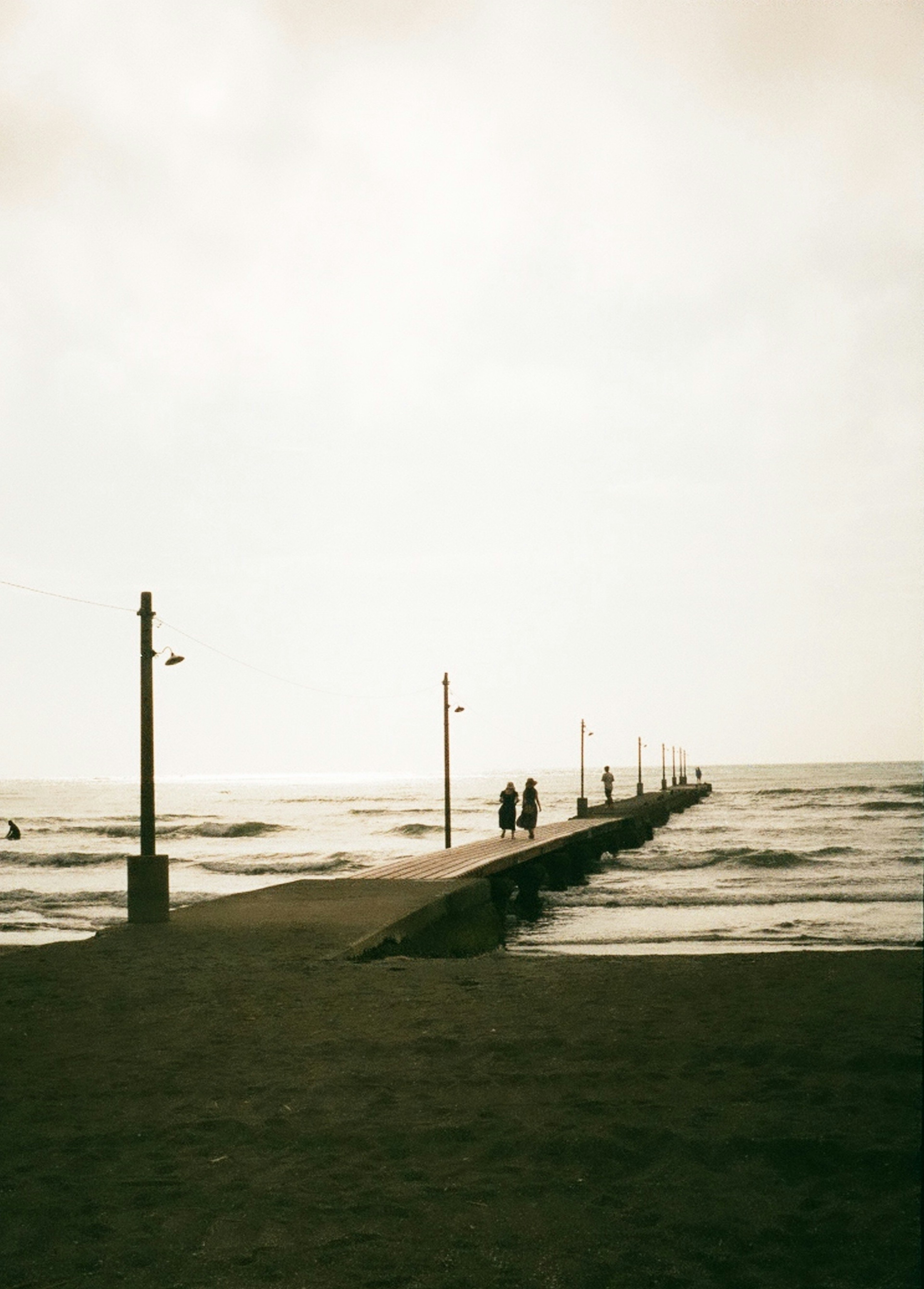 Silhouettes of people on a pier extending into the sea