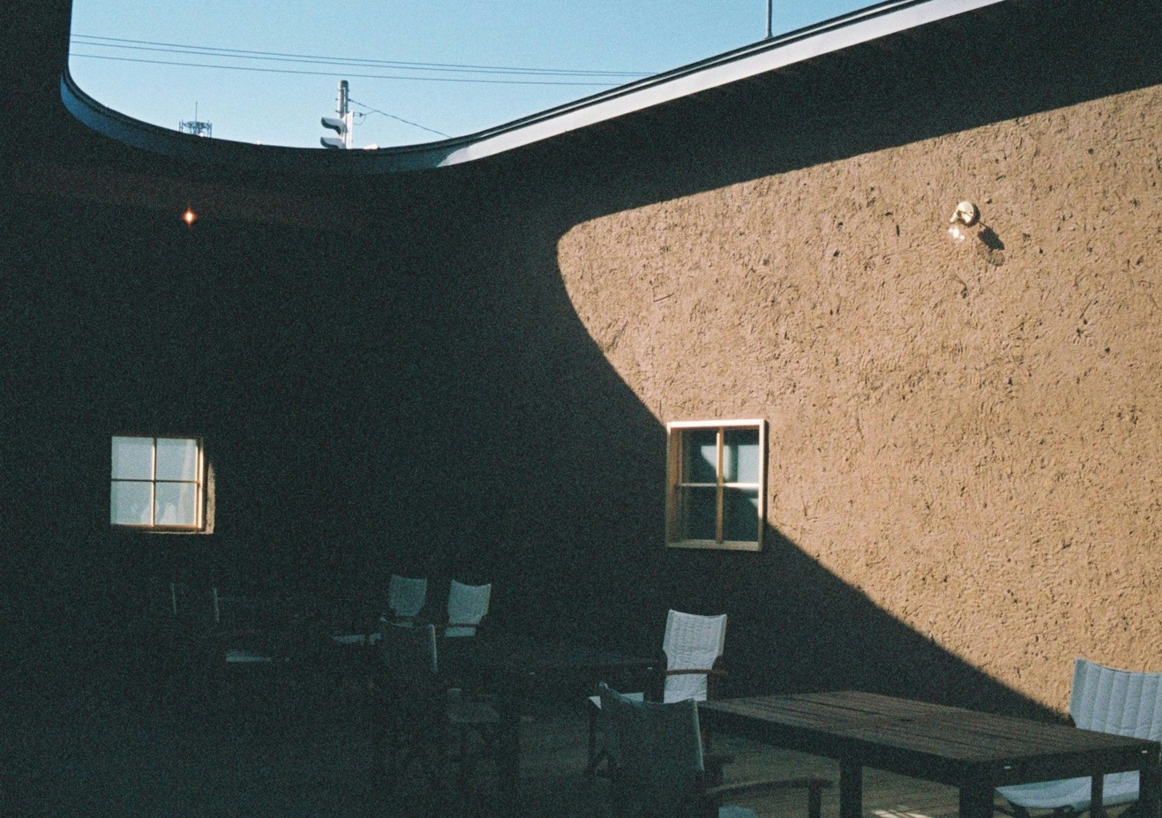 Outdoor terrace with white chairs and table Shadows cast on a textured wall